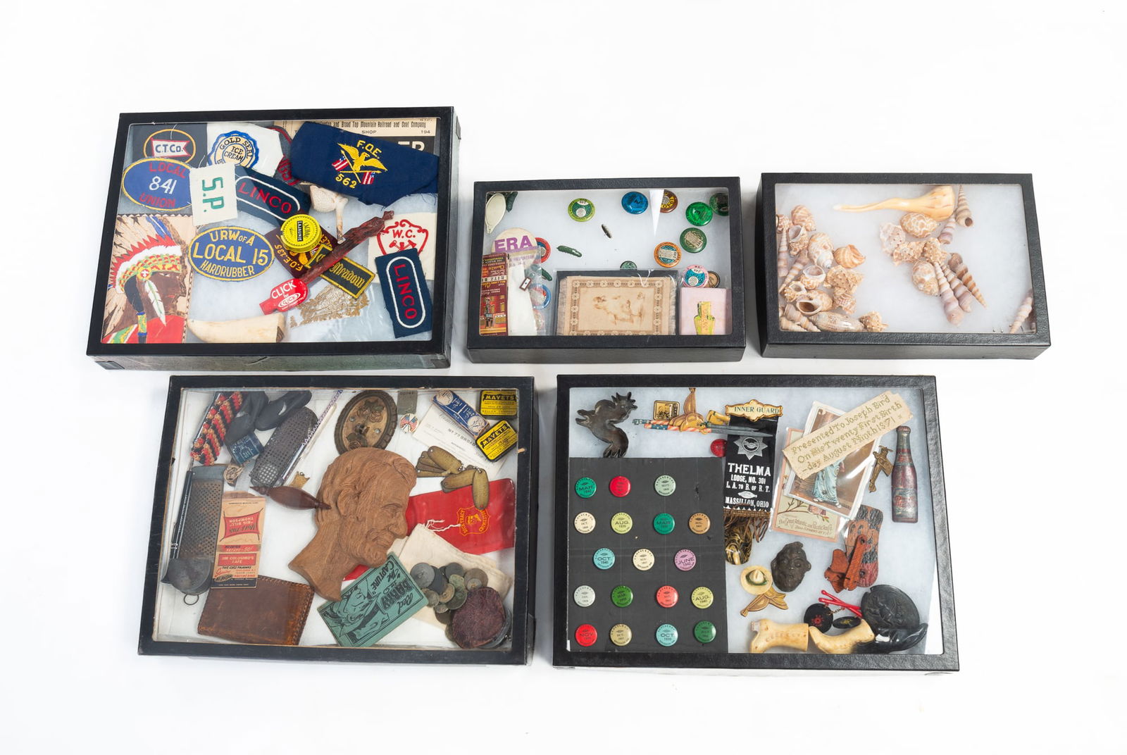 FIVE DISPLAY CASES FILLED WITH ECLECTIC ITEMS, INCL. RIBBONS, BUTTONS, AND COLLECTIBLES.: 20th Century. Includes patches, buttons, pins, tags, ribbons, a carved wood Lincoln head, seashells, and other curiosities.Provenance: From the Lifetime Collection of Chuck Auerbach. All together 11"h