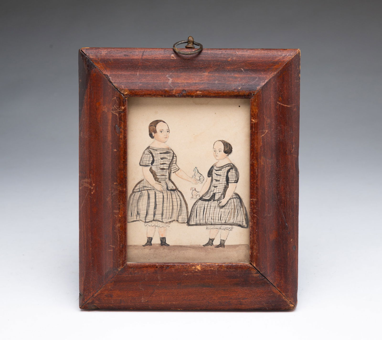 MINIATURE FOLK ART WATERCOLOR PORTRAIT OF TWO GIRLS WITH TOYS.: English or American, 19th Century. Two girls in checkered dresses, bloomers, and black booties, the taller one holding out a horse toy to the younger one, who is holding a dog toy. In a period molded