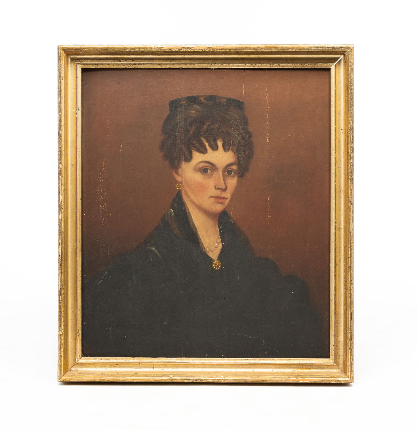 AMERICAN SCHOOL FOLK ART OIL ON BOARD PORTRAIT OF A WOMAN. Frame, 31.5"h. 27.25"w. Board, 27.75"h.: 19th Century. Red background, seated woman with her curly hair in an updo, wearing a black dress with a pearl necklace, pearl earrings and gold brooch. Unsigned. In a lemon gilt frame.Provenance: From