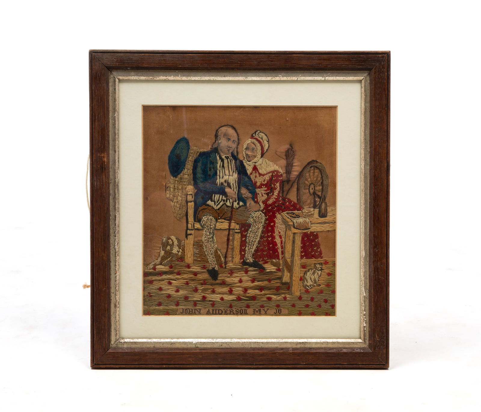 SCOTTISH WOOLWORK PICTURE OF A COUPLE WITH THEIR CAT AND DOG. Frame, 18"h. 17"w.: 19th Century. An older couple, he is seated on a chair with a dog on the floor behind him, she is seated at her spinning wheel next to a table that a cat sits under, stitched in polychrome wool and wi