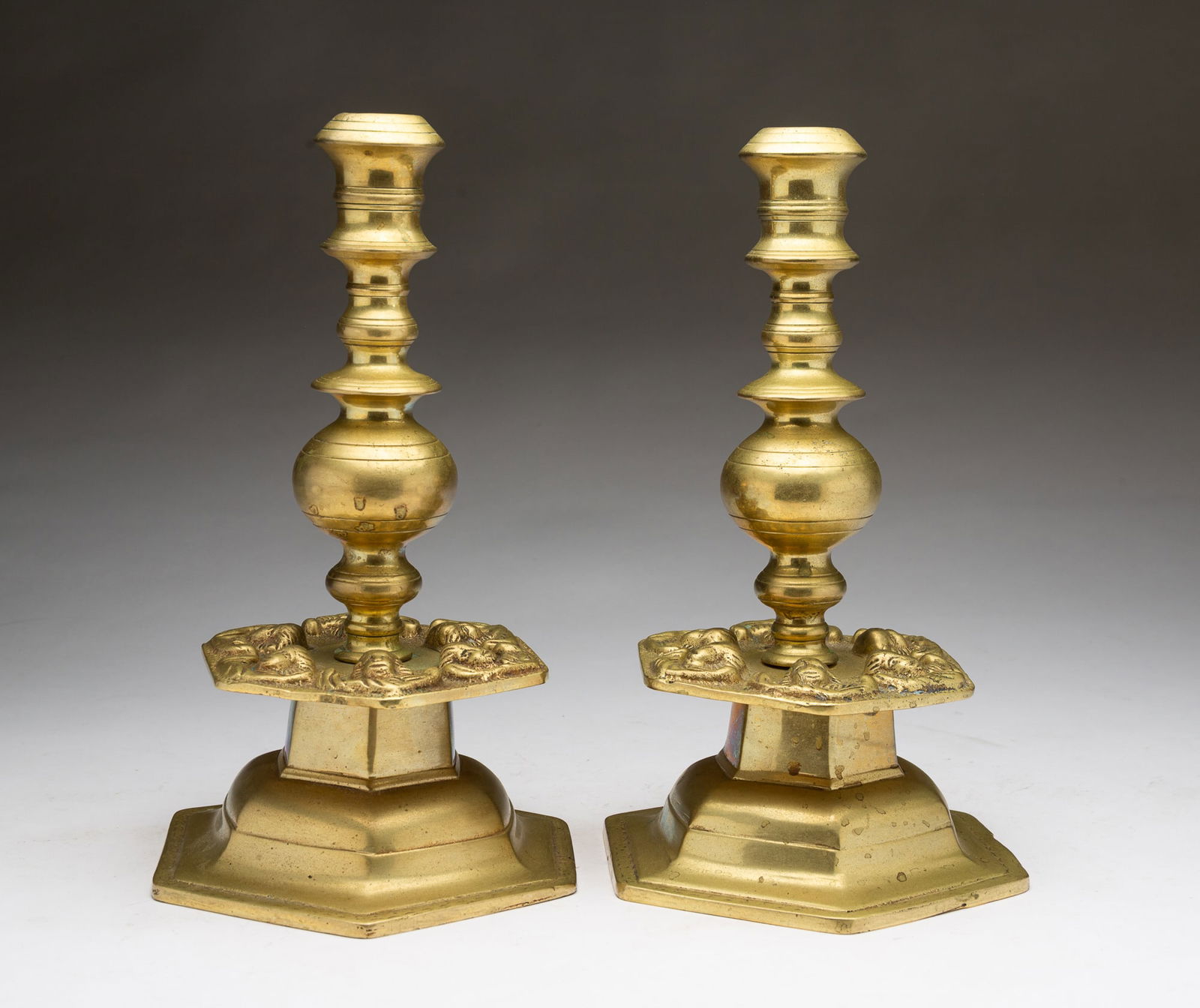 PAIR OF SCANDINAVIAN BAROQUE-STYLE FIGURAL CHERUB MASK BRASS CANDLESTICKS. Each, 11"h. 7"w. 7"d.: 20th Century. Large sockets, with ball standard, hexagonal drip tray with cherub masks and wings, a large hexagonal base, in three parts.SHIPPING: All purchases from Amelia Jeffers, Auctioneers & Appr