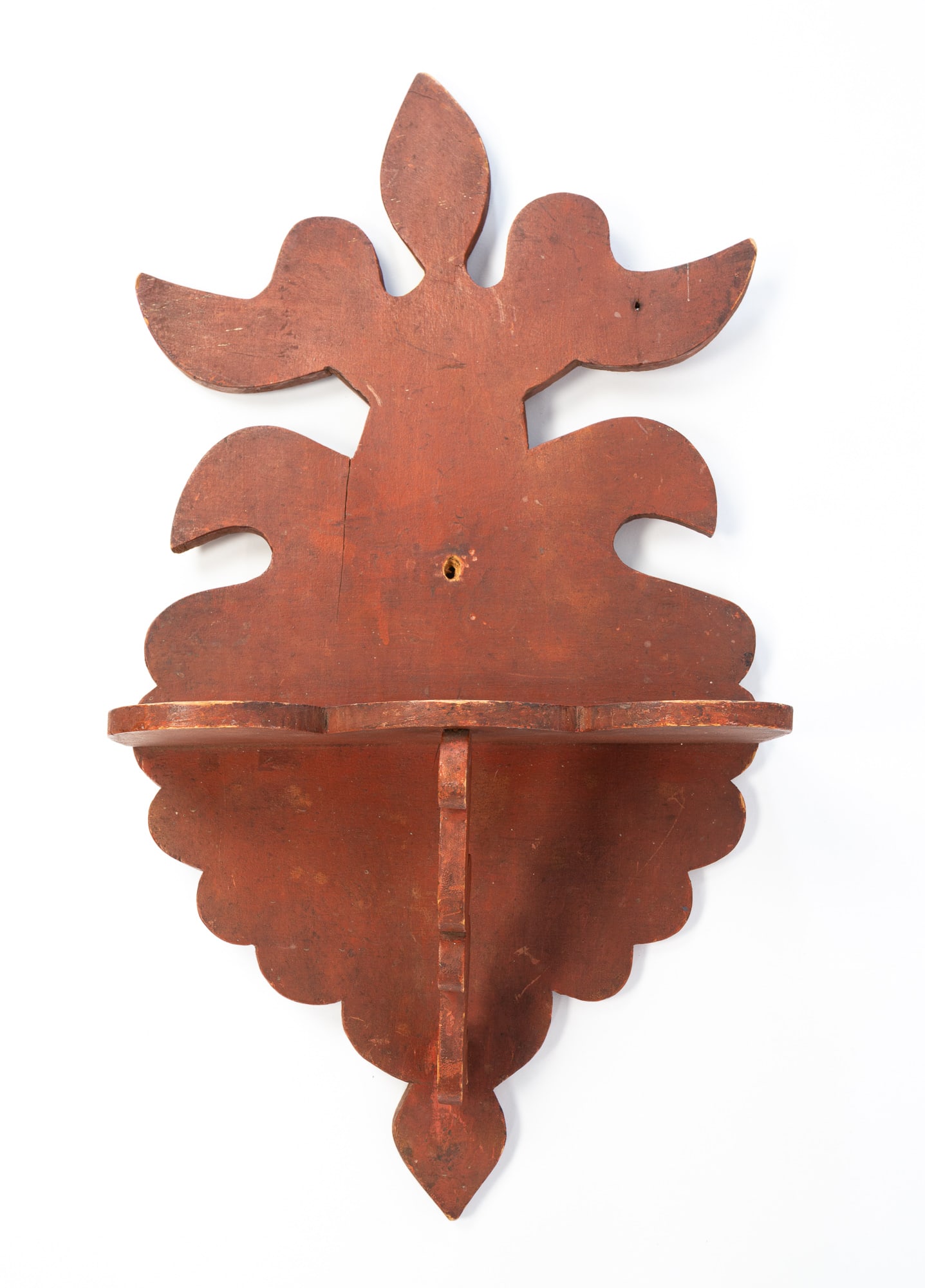 AMERICAN FOLKSY RUST RED-PAINTED PINE HANGING SHELF. 25"h. 13.75"w. 6"d.: Second half 19th Century. Leafy crest, scalloped base and shelf, scrolled shelf support, and original paint.SHIPPING: All purchases from Amelia Jeffers, Auctioneers & Appraisers may be picked up by