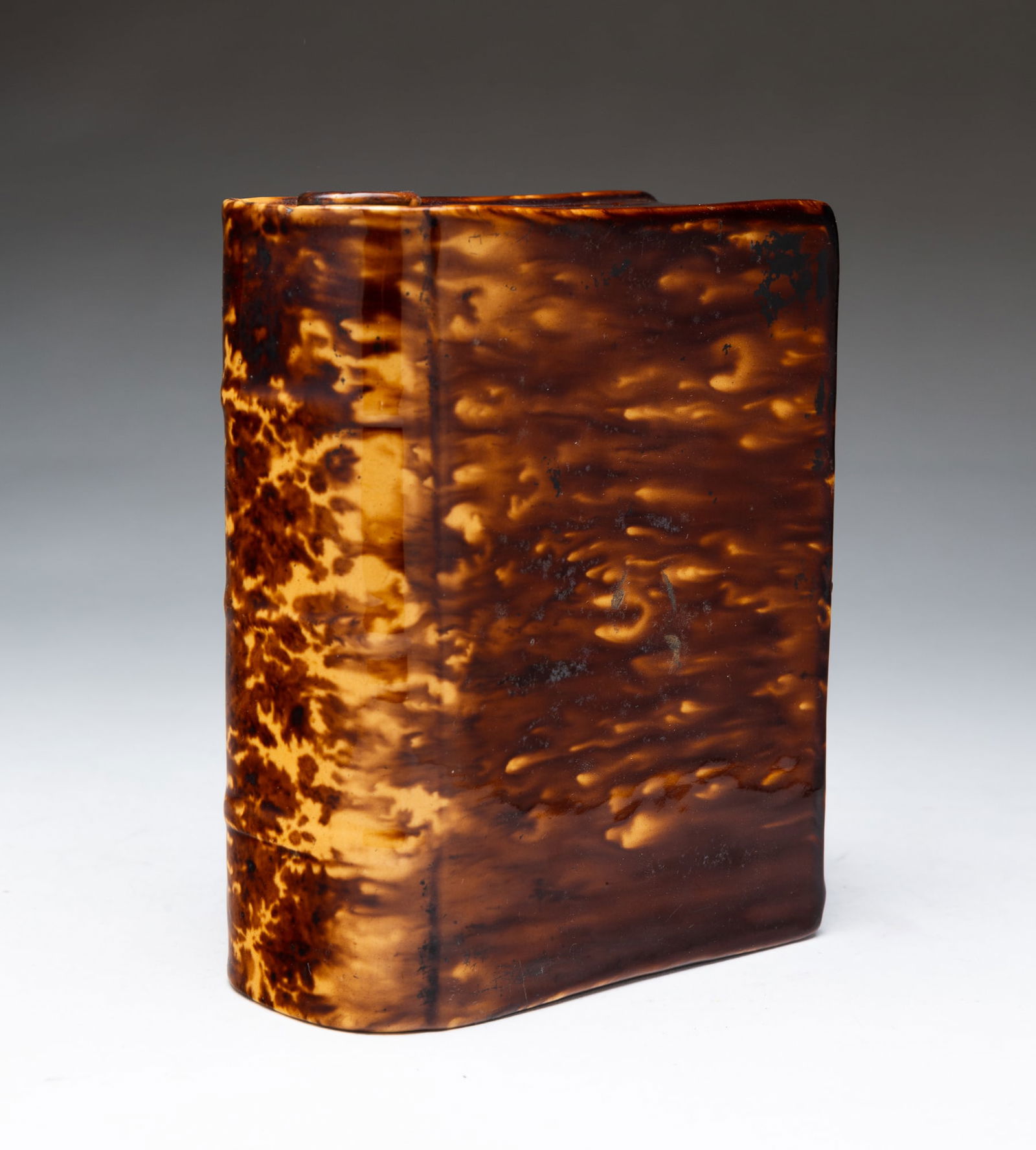 ENGLISH ROCKINGHAM YELLOWWARE BOOK FLASK. 6.75"h. 5.5"w. 2.5"d.: Mid-19th Century. Nicely shaped with ribbed spine and mottled brown Rockingham glaze.SHIPPING: All purchases from Amelia Jeffers, Auctioneers & Appraisers may be picked up by you or your designated