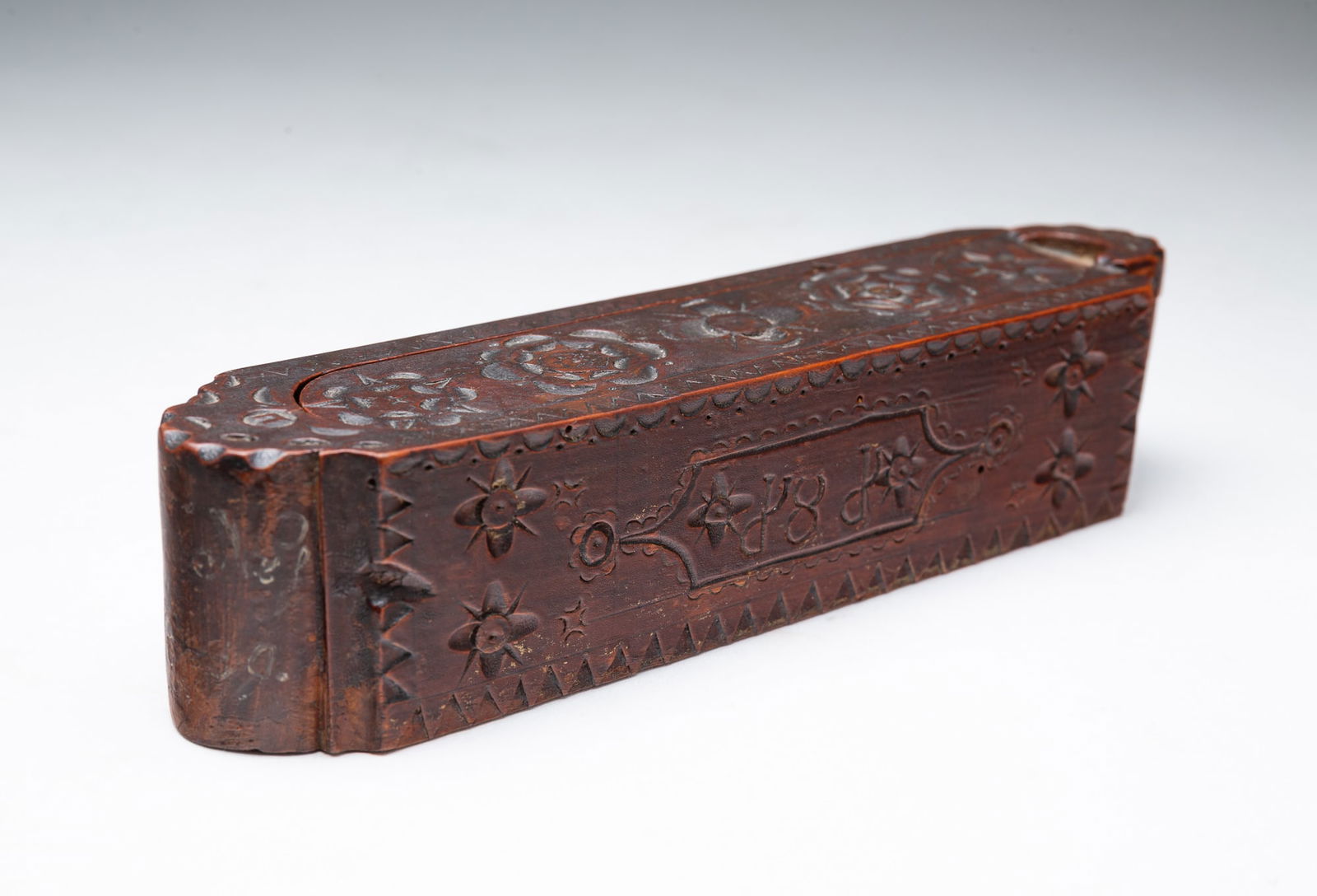 AMERICAN FOLK ART CHIP-CARVED BOX, DATED 1839. 1.75"h. 8"w. 1.75"d.: Carved from one piece of wood. Rectangular with rounded ends, slide lid pinwheel, floral and saw tooth carving, on one side in a panel are initials "A.F.K." on reverse in matching panel are three