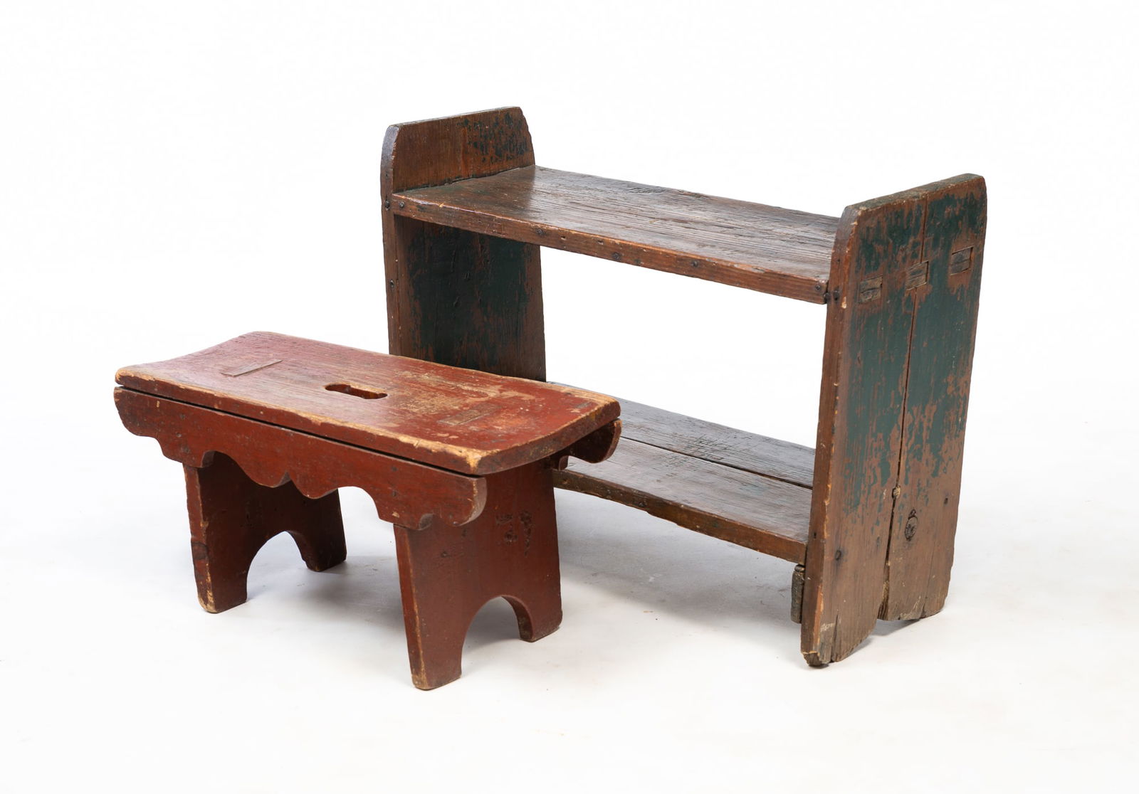 AMERICAN DARK GREEN-PAINTED PINE TWO-TIER SHELF AND RUST RED-PAINTED PINE STOOL.: Mid-19th Century. Diminutive pine two-tier shelf, boot jack ends, mortise and square nail construction, and worn original dark green paint. 19.5"h. 27"w. 9.5"I. And a pine stool, legs with half-round
