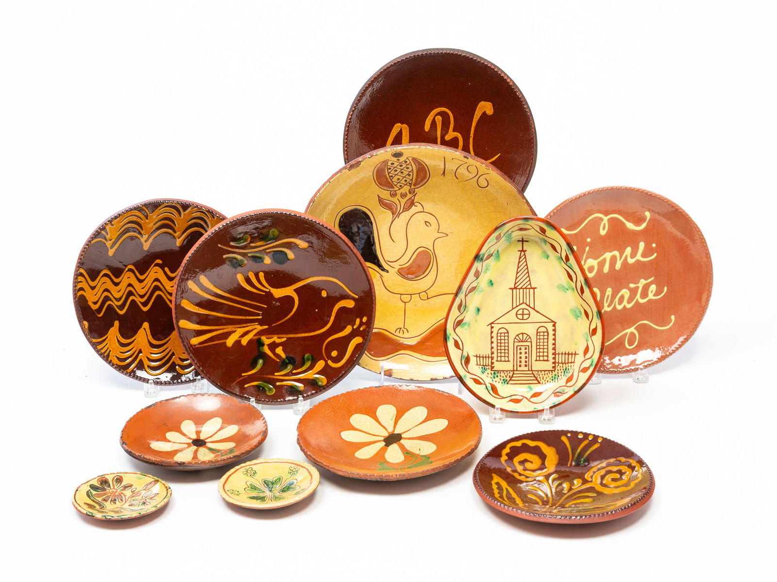 ELEVEN AMERICAN REDWARE ITEMS, INCL. TURTLE CREEK POTTERS (MORROW, OHIO). Largest, 11.75"d.: Contemporary. Five are Turtle Creek Potters, Morrow, Ohio. Two floral cup plates with yellow glaze, two plates with coggled rims and daisies, 6.25" d. and 8" d., and a large plate with bird, flower, a