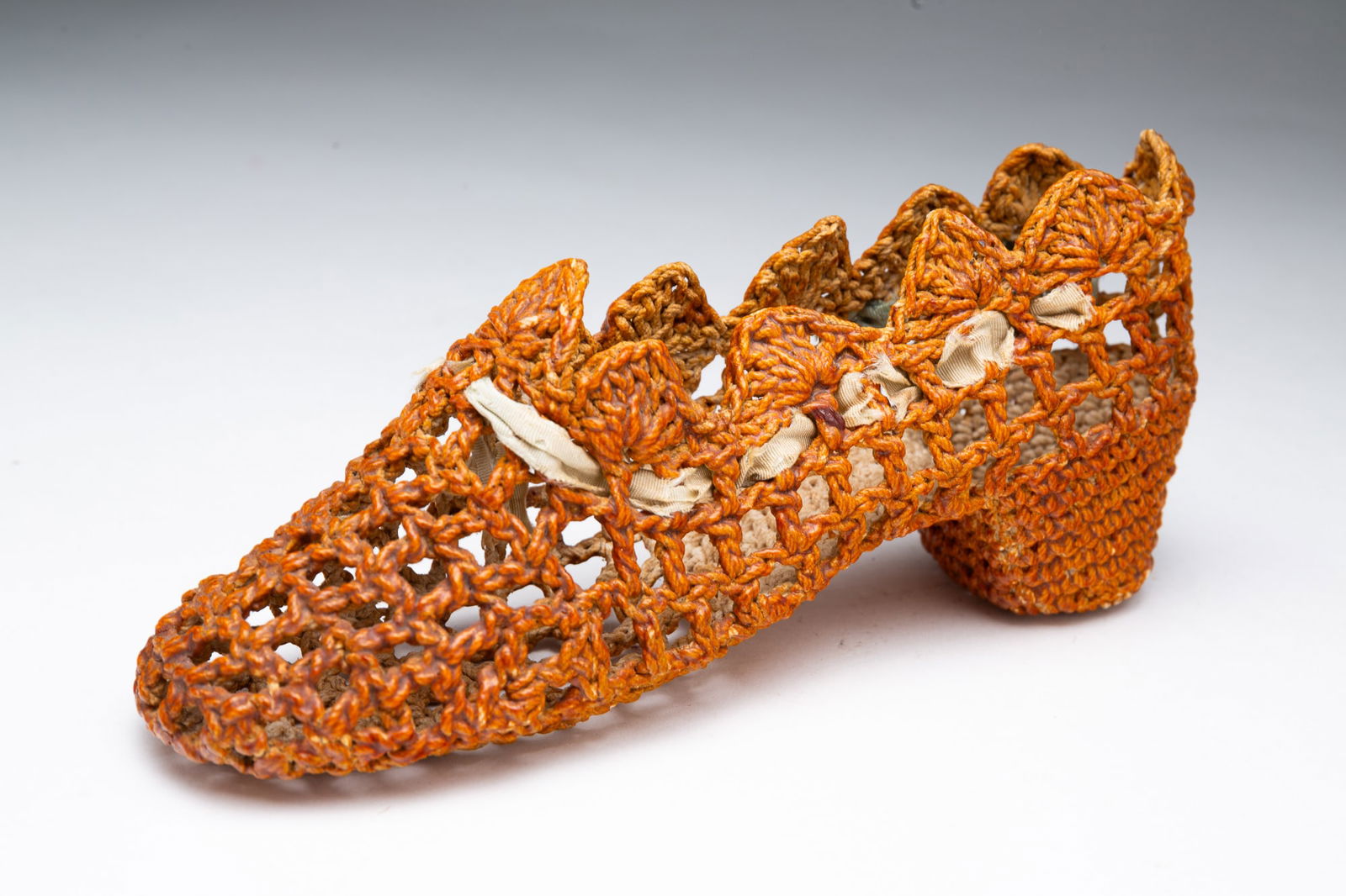 AMERICAN FOLK ART SAILOR-MADE MACRAME SHOE. 3.75"h. 8"l.: Late 19th Century. Sailor-made shoe whimsey, macrame from small nautical rope with scalloped edges, sensible heel, and decorated woven ribbon.Provenance: From the Collection of Peggy McClard & Randy S