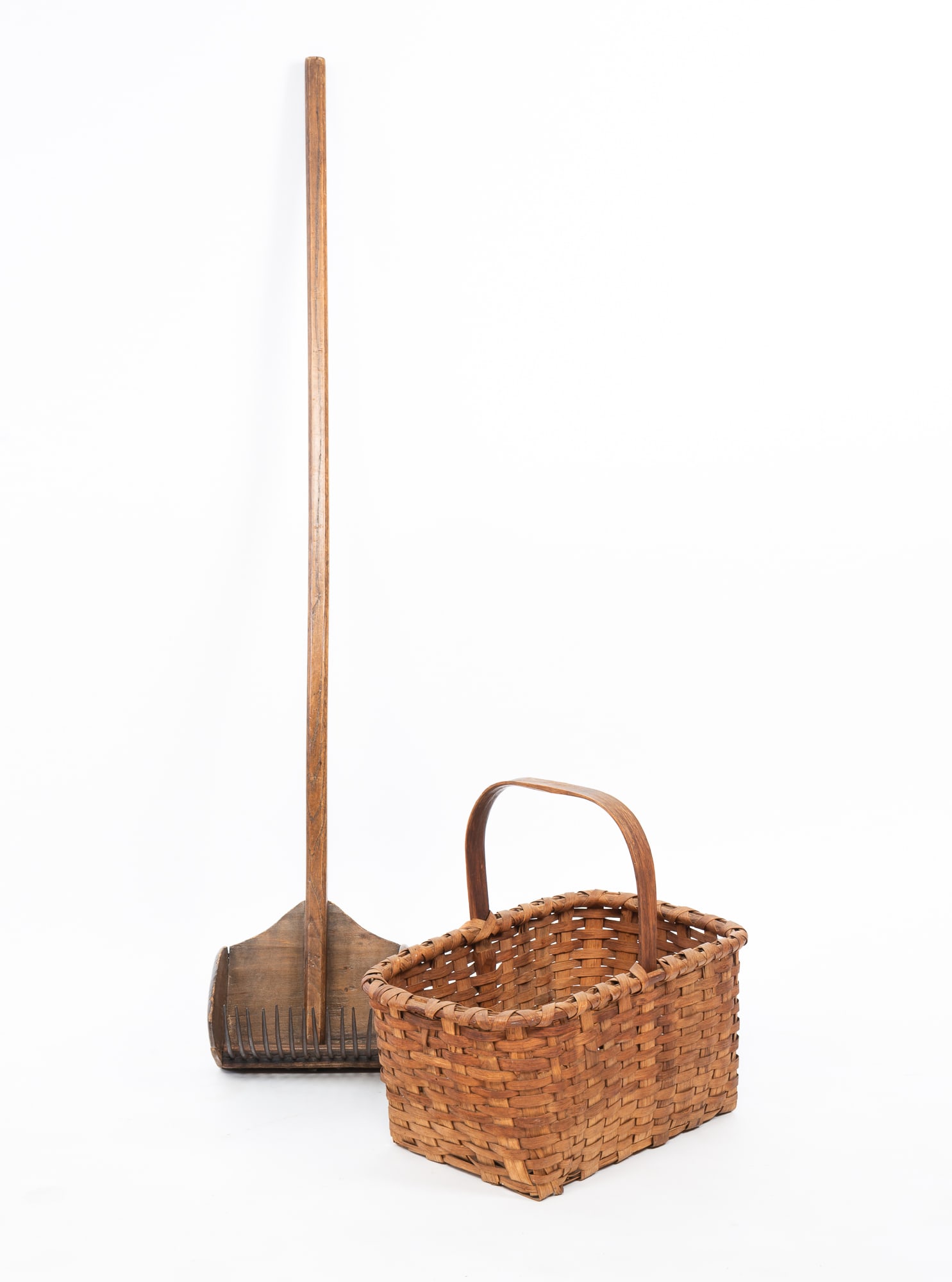 AMERICAN CRANBERRY SCOOP AND SPLINT-WOVEN BASKET. Scoop, 44"h. 8"w. 7"d. Basket, 13.5"h.: Ca. 1900. Long handled oak and poplar scoop with steel tines and an oak splint rectangular basket with arched handle.Provenance: The Lifetime Collection of Phil Florence & the late C.J. Hawley.SHIPPIN