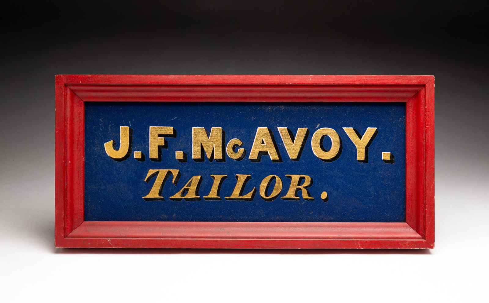AMERICAN SANDED "J.F. MCAVOY TAILOR" TRADE SIGN. 8.5"h. 18.5"w.: Fourth quarter 19th Century. Having gilt lettering with black drop shadows on blue smaltz ground and presented in a red frame.SHIPPING: All purchases from Amelia Jeffers, Auctioneers & Appraisers may