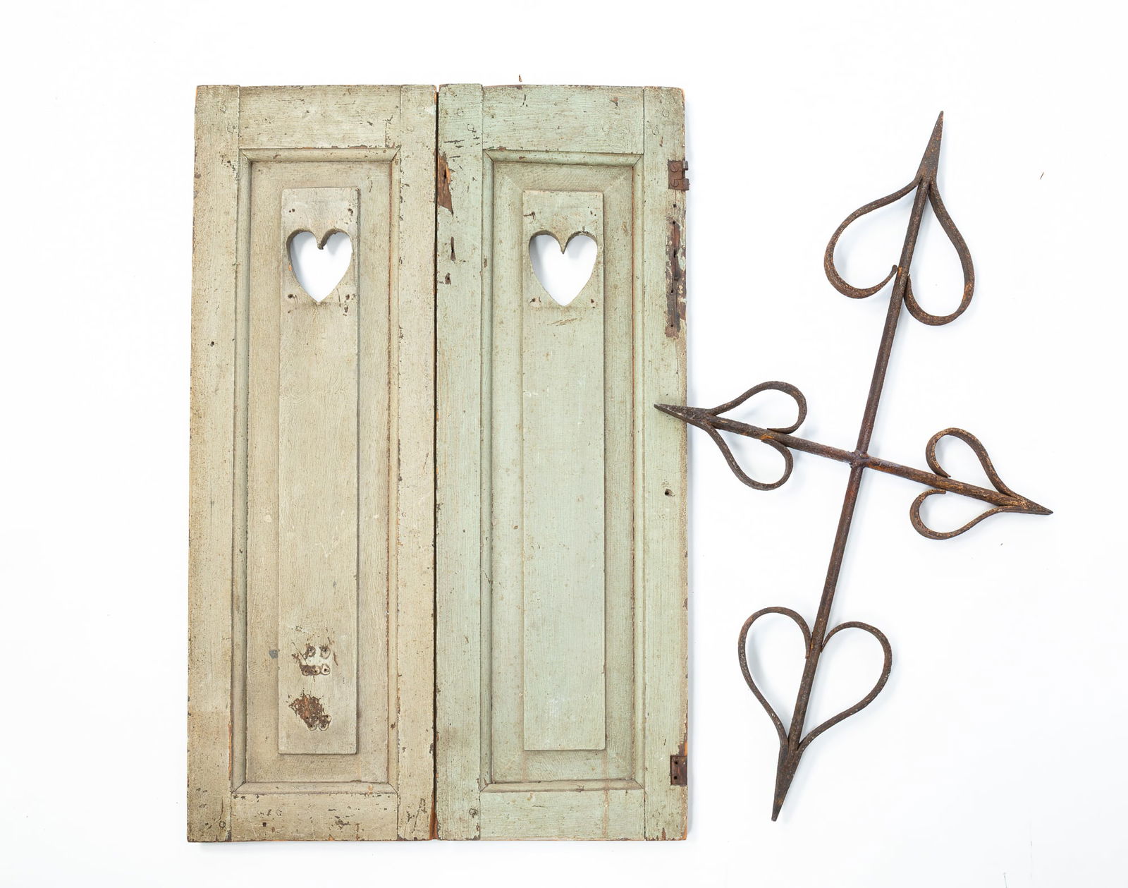 PAIR OF PAINTED PINE SHUTTERS WITH CUTOUT HEARTS AND A WROUGHT IRON ARCHITECTURAL ELEMENT. Shutters,: American, 19th Century. Pair of pine shutters in gray-green paint and heart cut-outs on raised panels, and a wrought iron heart architectural element.SHIPPING: All purchases from Amelia Jeffers, Aucti