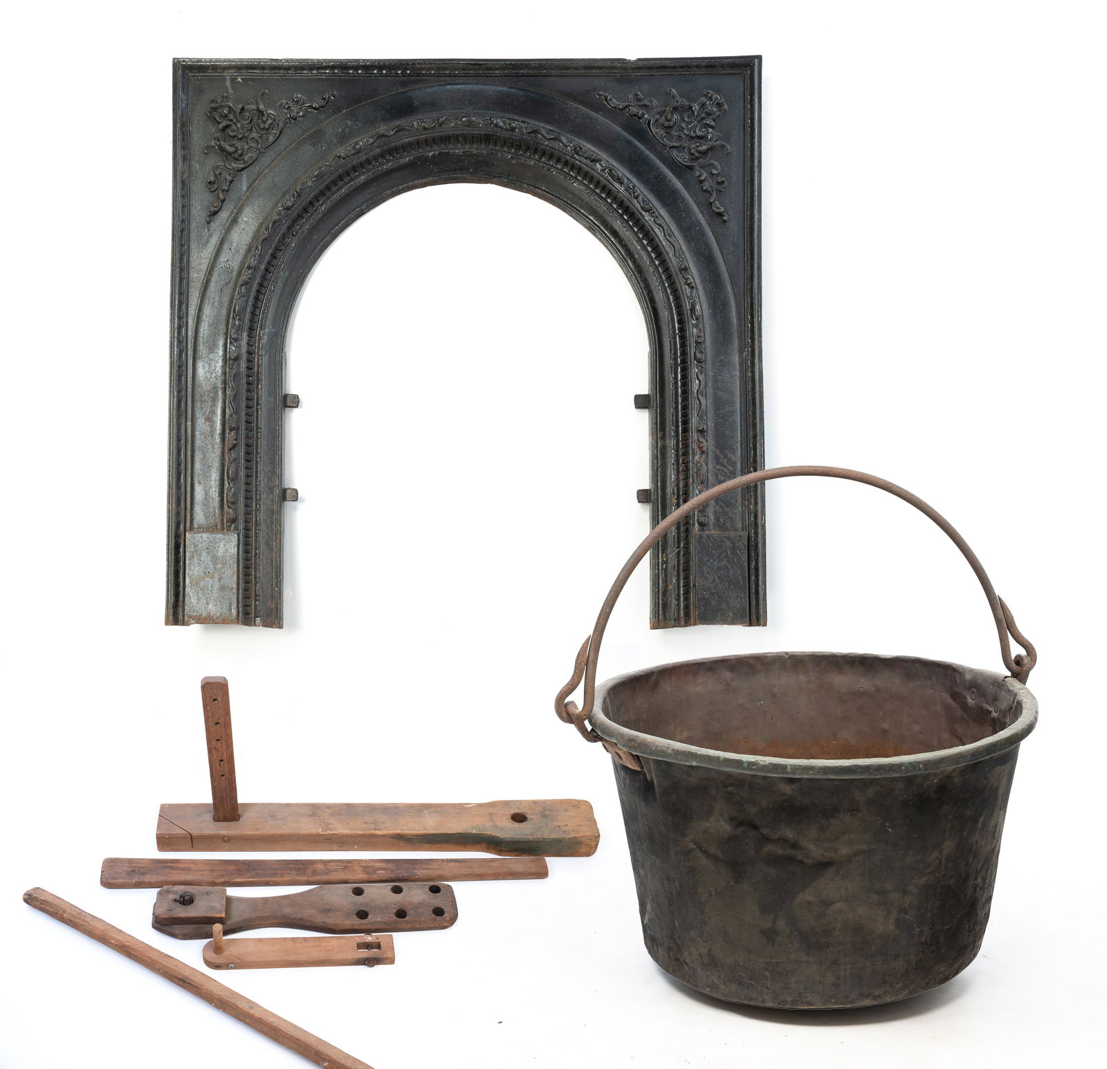 AMERICAN CAST IRON FIREPLACE SURROUND WITH A COPPER KETTLE AND WOODEN TOOLS. Fireplace surround,: Mid-19th Century. A fireplace surround with nicely cast detail with arched opening.An apple butter stirring paddle, tool with a dowel on end, clamp remnant, and two boards. Largest, 33"l. And a kettle