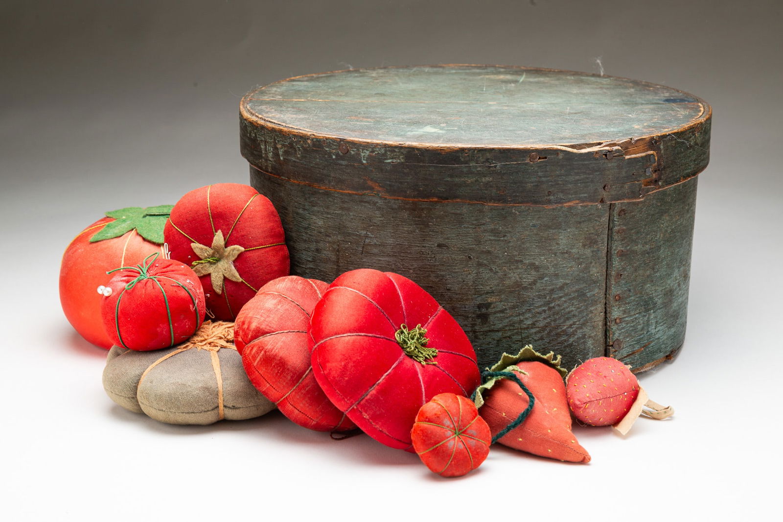 LARGE AMERICAN BLUE-PAINTED BENTWOOD PANTRY BOX FILLED WITH STRAWBERRY AND TOMATO-FORM PINCUSHIONS.: 19th Century. Round lidded pantry box with lapped construction and old nails, filled with nine pincushions of strawberry and tomato forms.SHIPPING: All purchases from Amelia Jeffers, Auctioneers & App