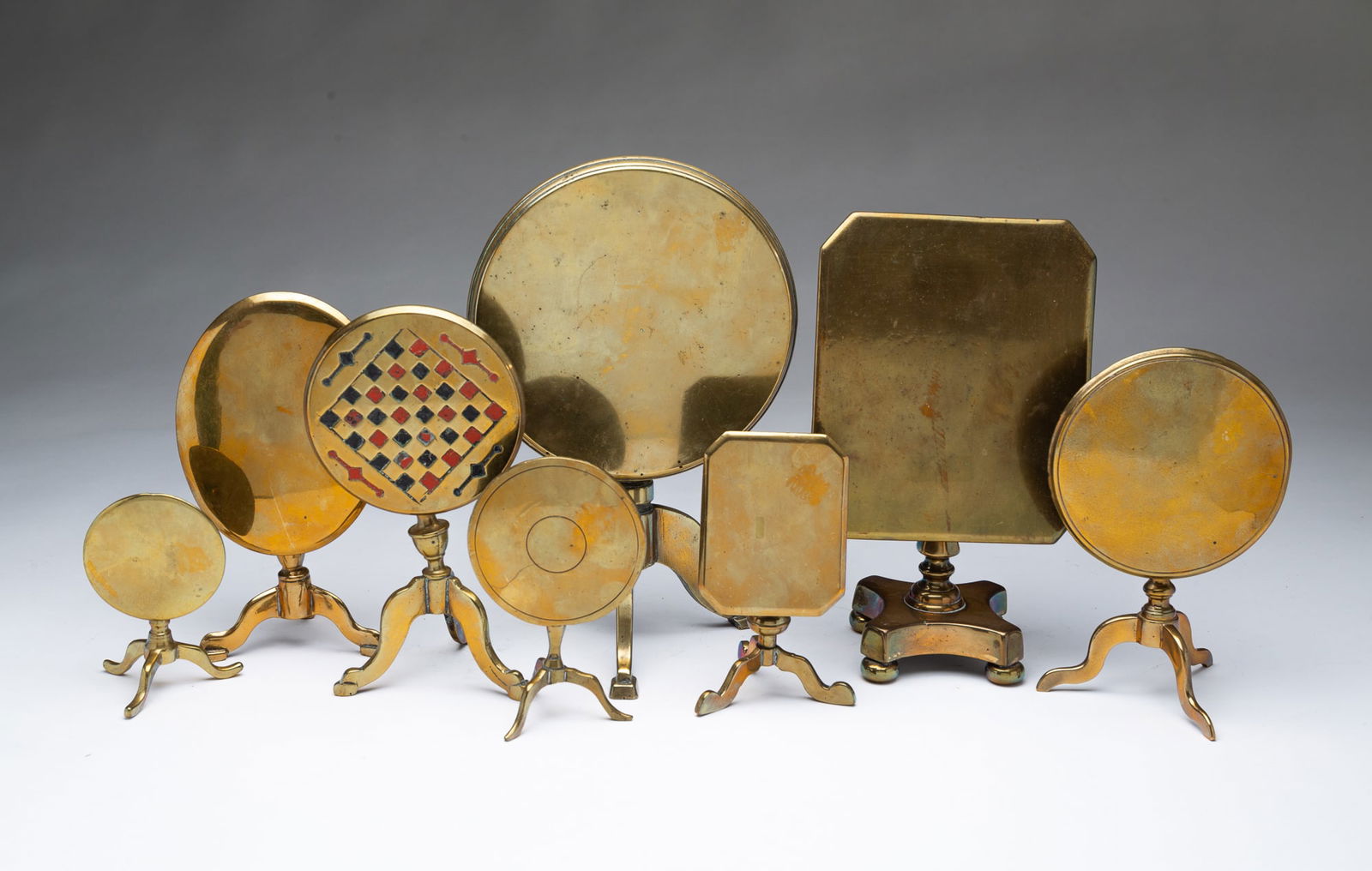 EIGHT ENGLISH BRASS MINIATURE TILT-TOP TABLE/CANDLE REFLECTORS. Largest, 7"h. 6"d.: 19th Century. Five are round on tripod bases, one with a checkerboard top, two have rectangular tops with cut corners, and one has an oval top.SHIPPING: All purchases from Amelia Jeffers, Auctioneers