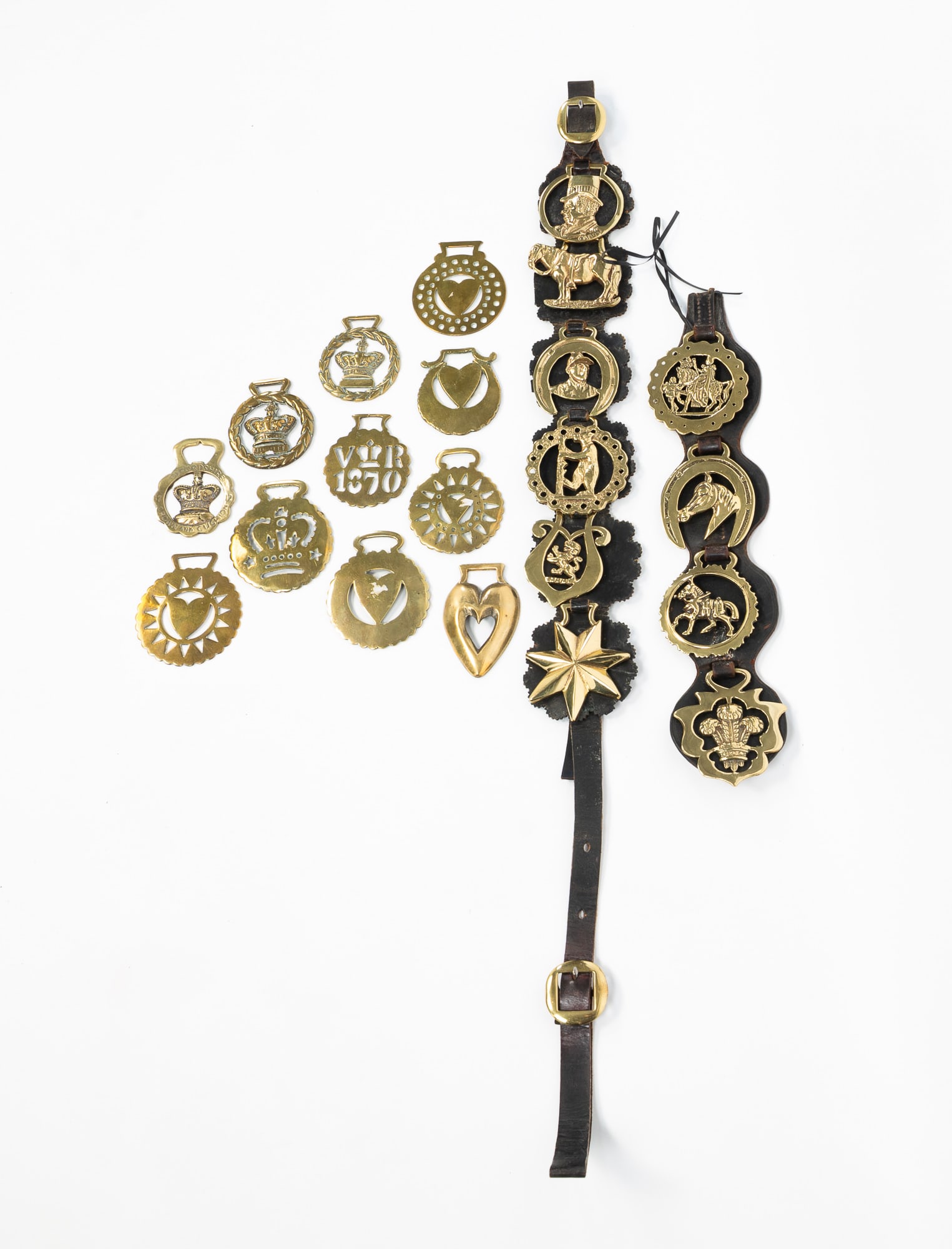 LARGE GROUP OF HORSE BRASSES. Largest strap, 39"l.: English, 19th Century. Includes two leather straps mounted with brasses, and eleven loose brasses. Featuring hearts, crowns, and other motifs.SHIPPING: All purchases from Amelia Jeffers, Auctioneers &