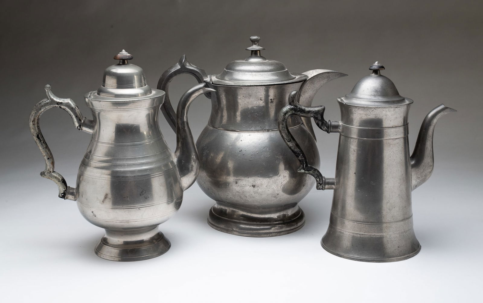 THREE AMERICAN PEWTER ITEMS. Largest, 12"h.: First half 19th Century. A R. Gleason cider jug, bulbous body, scrolled handles, low-domed lid with finial, and low foot. A R. Dunham lighthouse-shaped coffee pot with gooseneck spout, scrolled handle