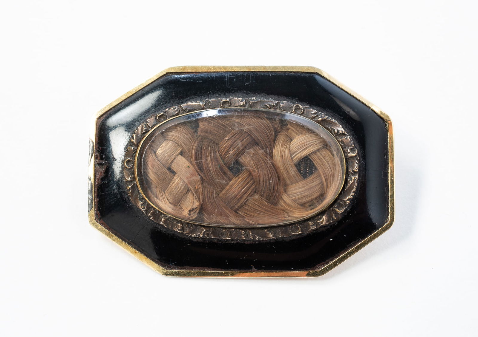 14K YELLOW GOLD AND ENAMEL HAIR-WORK MOURNING BROOCH. 1.25"h. 1.75"w.: American, Second half 19th Century. Unmarked. 14k yellow gold octagonal brooch with black enamel and a viewing window showing intricately braided hair. Approximately 11.3g.SHIPPING: All purchases