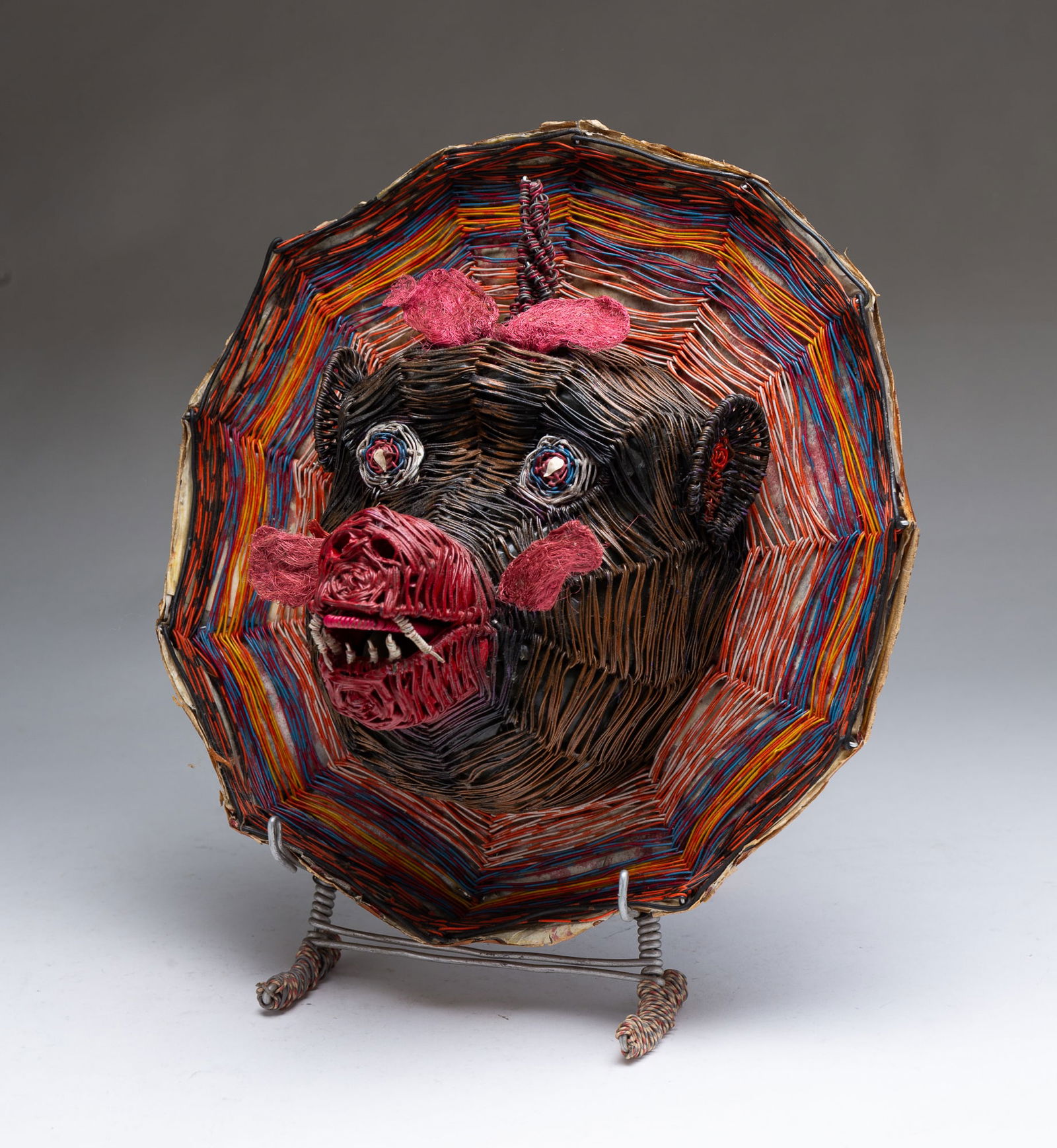 W.D. "CRAZY MAC" MCCAFFREY (AKRON, OHIO, 1923 - 1993) OUTSIDER ART COLORED WIRE BABOON HEAD PLAQUE.: American, 20th Century. A brown baboon head with a horn and pink accents on a multi-colored circular background. Signed to back. On a wire stand.Provenance: From the Lifetime Collection of Chuck Auerb