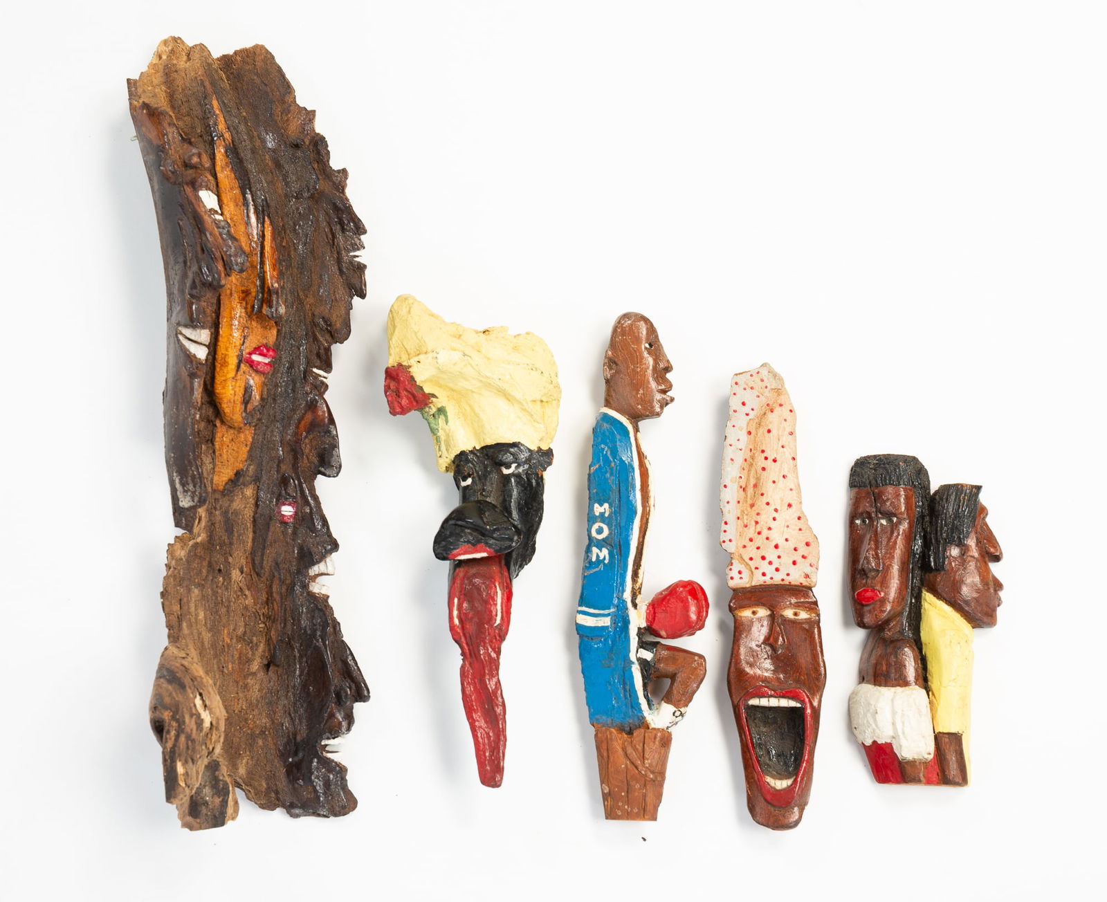 FIVE RON COLLINS (AKRON, OHIO) BLACK AMERICANA BARK CARVINGS. Largest, 17.5"h. 5.5"w.: American, 20th Century. A seated boxer in a blue robe, a couple seated back to back, a man with a cap and his tongue sticking out, a person wearing a polka-dotted hat with their mouth open, and a piec