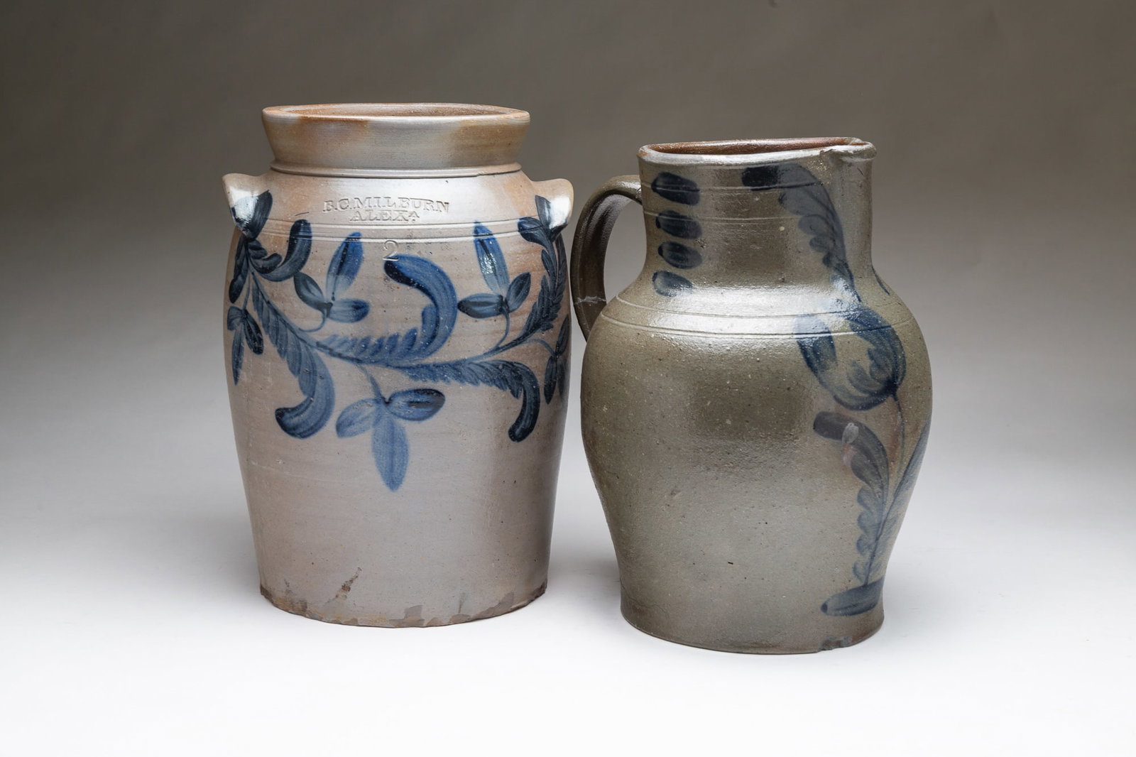 TWO AMERICAN COBALT-DECORATED STONEWARE VESSELS, INCL. B.C. MILBURN (ALEXANDRIA, VIRGINIA).: Mid-19th Century. Pitcher having a pinched spout, applied strap handle, tooled shoulder, and freehand cobalt flowers and flourishes. 11.5"h. 9"w. B.C. Milburn (Alexandria, Virginia) jar having a