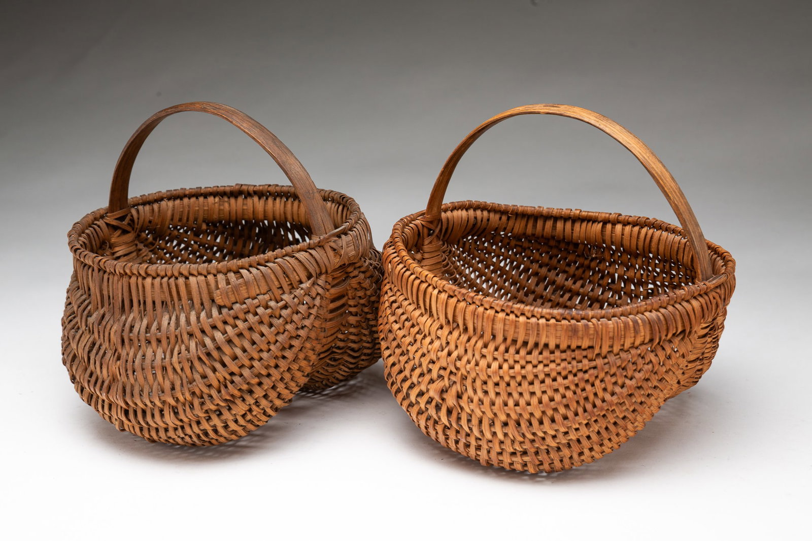 TWO AMERICAN SPLINT-WOVEN BUTTOCKS BASKETS.: Ca. 1900. Both with wrapped rims and bentwood handles, of differing natural colors. The larger, 6.5"h. 6.25"w. 6.5"d.Provenance: From the late George Shahady (Bridgeport, West Virginia).