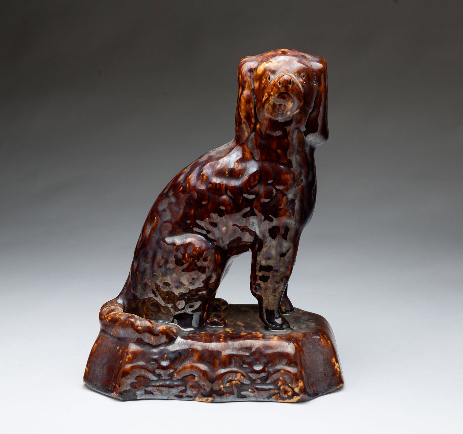 AMERICAN ROCKINGHAM-GLAZED YELLOWWARE SEATED SPANIEL.: Mid-19th Century. Seated spaniel on a plinth with shaped corners. 11"h. 8"w. 5"d.