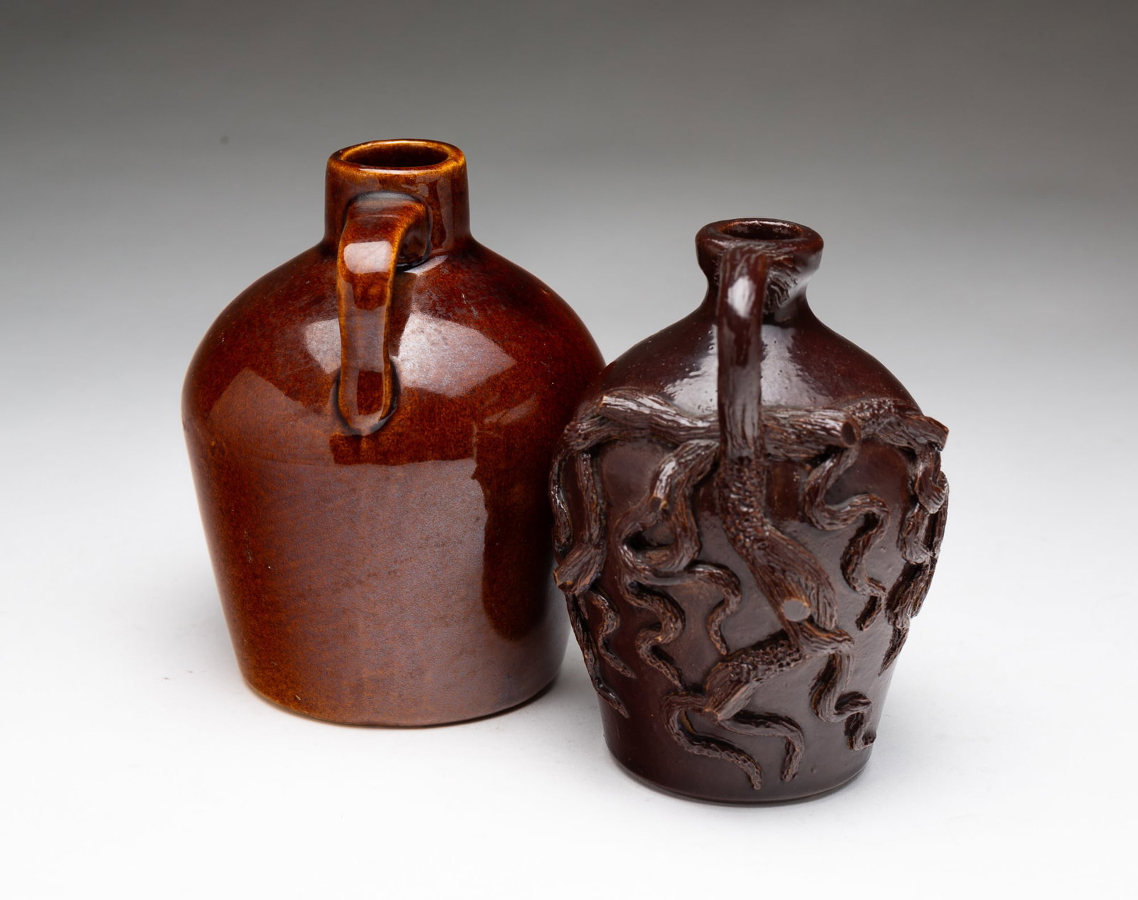 TWO MINIATURE AMERICAN JUGS, INCL. ROYCROFT (EAST AURORA, NEW YORK) AND BRANCH-AND-SNAKE EXAMPLES.: American, Early 20th Century. Sewer tile with Albany glaze, the handle decorated like a branch with applied and textured branches and snakes on the sides. 4.5"h. Roycroft Albany slip jug, marked on