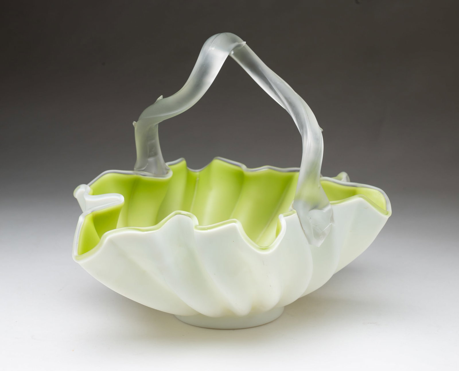 AMERICAN VICTORIAN ART GLASS BASKET.: AMERICAN VICTORIAN ART GLASS BASKET. Late 19th Century. Pistachio-colored glass cased in white bowl with ribbed sides and ruffled rim. Thorn handle, acid-etched finish, and ground pontil. 9"h. 11.25"w