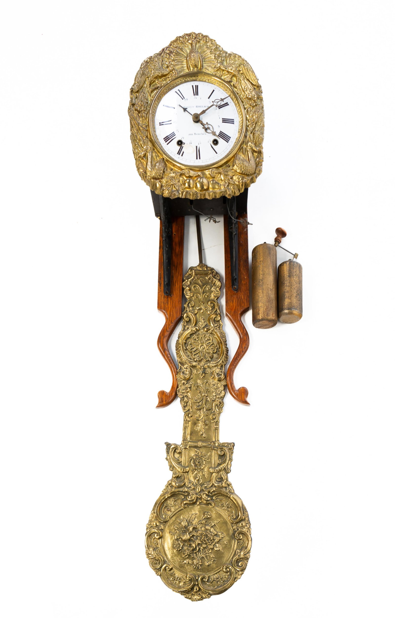 FRENCH WAG ON THE WALL CLOCK.: Mid-19th Century. Heavily embossed face surround and pendulum, white enameled face lettered "Hippolyte Rilland, aux Touches", brass works, sheet metal case, weights, and key. Includes oak wall mount b