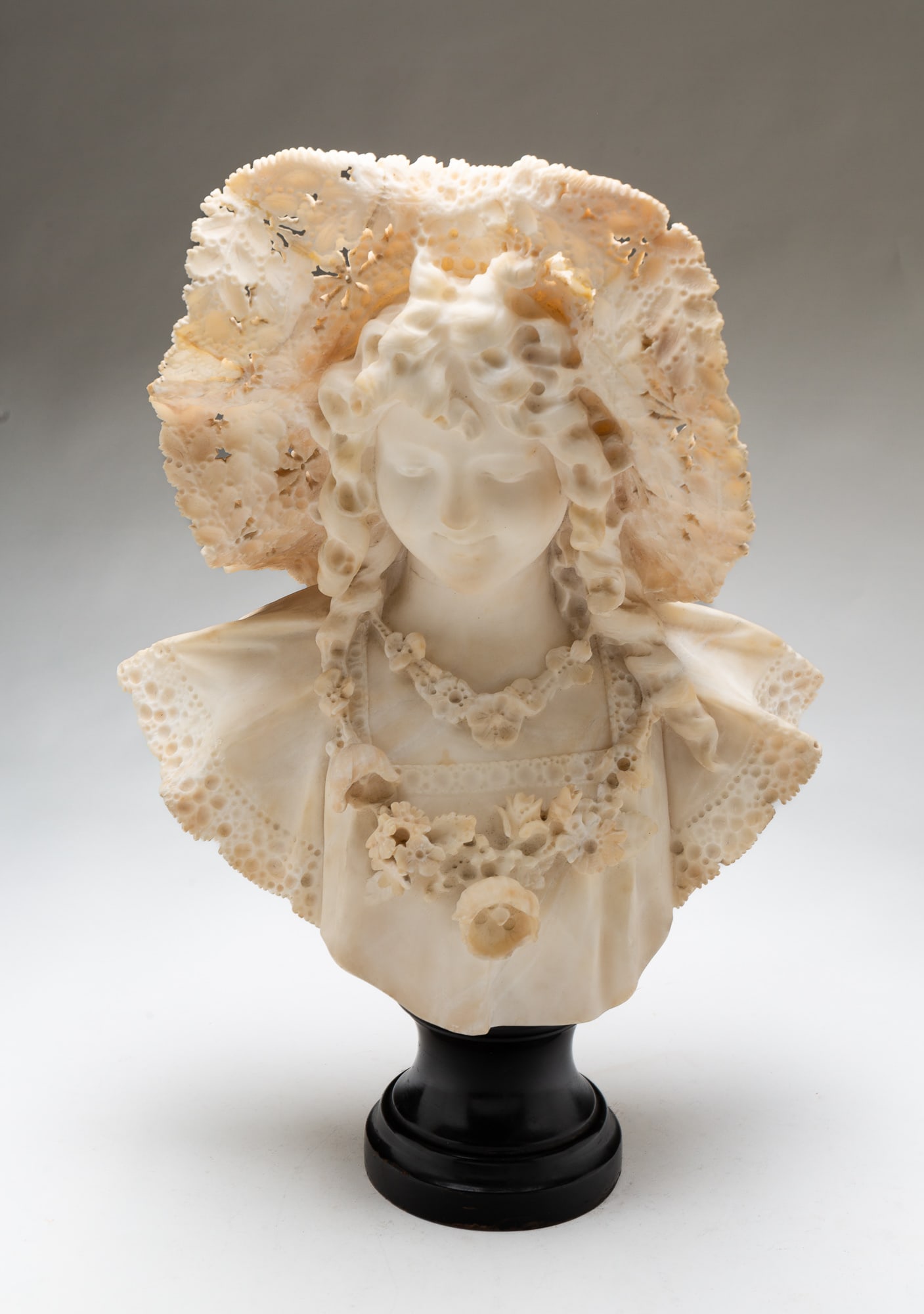ADOLFO CIPRIANI (FLORENCE, ITALY, 1857-1941) MARBLE BUST OF A LADY.: Ca. 1900. Young lady in a pierced carved lacy hat, long curls, and wearing a dress with lace collar and sleeves adorned with a floral necklace. Signed on reverse "A. Cipriani, Firenze". 22.5"h.