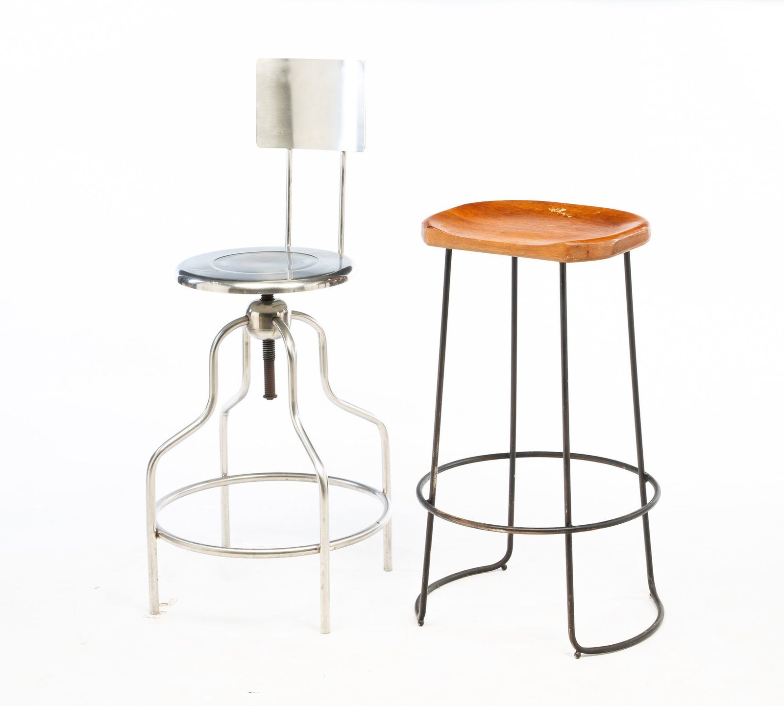 TWO INDUSTRIAL STOOLS, INCL. DRAFTING EXAMPLE.: American, 20th Century. Stainless steel stool with backrest and swivel seat. 41"h. 26.5" seat h. 20.75"dia. Other stool with shaped wood seat and wrought iron base. 31"h. 18.5"dia.Provenance: From the
