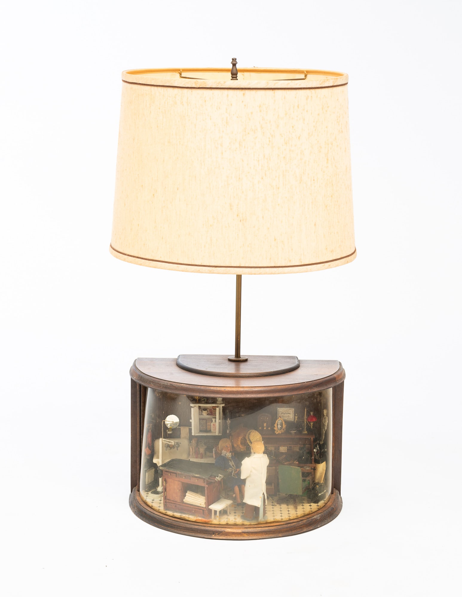 MINIATURE ROOM DIORAMA OF AN OBGYN OFFICE/LAMP.: American, 20th Century. A table lamp with a diorama base. The diorama shows the OBGYN office of Mr. Robertson with a pregnant patient in a seat and the doctor getting ready to administer a shot. 30"h.
