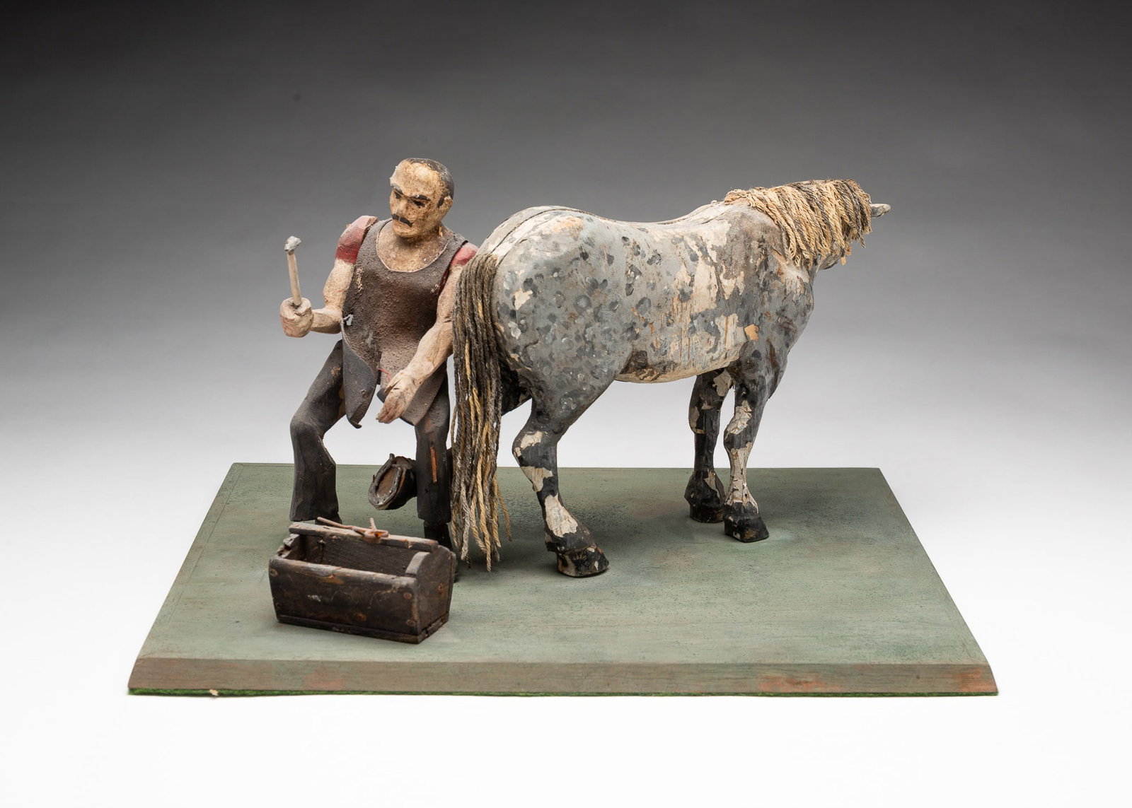 AMERICAN FOLK ART CARVED AND PAINTED WOOD SCULPTURE OF A HORSE AND FARRIER.: 19th Century. Dappled gray horse standing with back hoof exposed to farrier who is replacing the horseshoe, on a painted plinth base. 7.5"h. 14"w. 11"d. Provenance: From the Lifetime Collection of