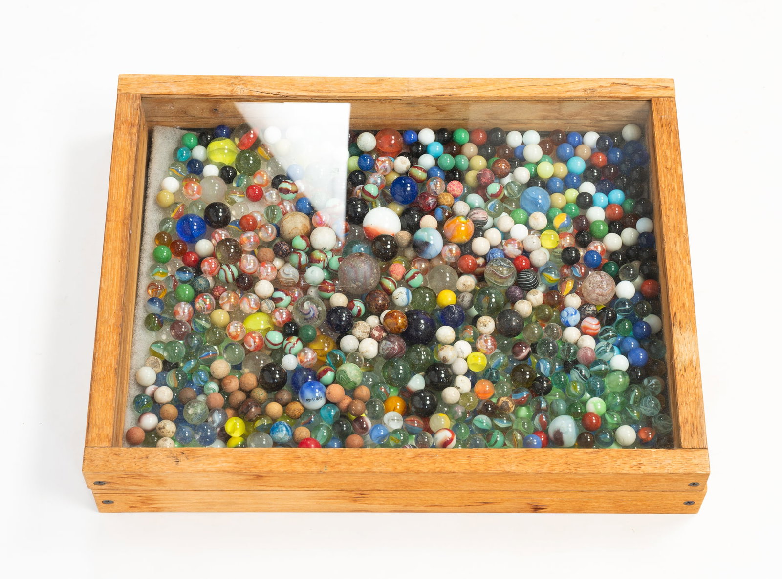 LARGE COLLECTION OF MARBLES.: American, 20th Century. Mostly all glass, some clay. Various sizes and colors, housed in a wood box with a glass lid.Provenance: From the Lifetime Collection of Chuck Auerbach.