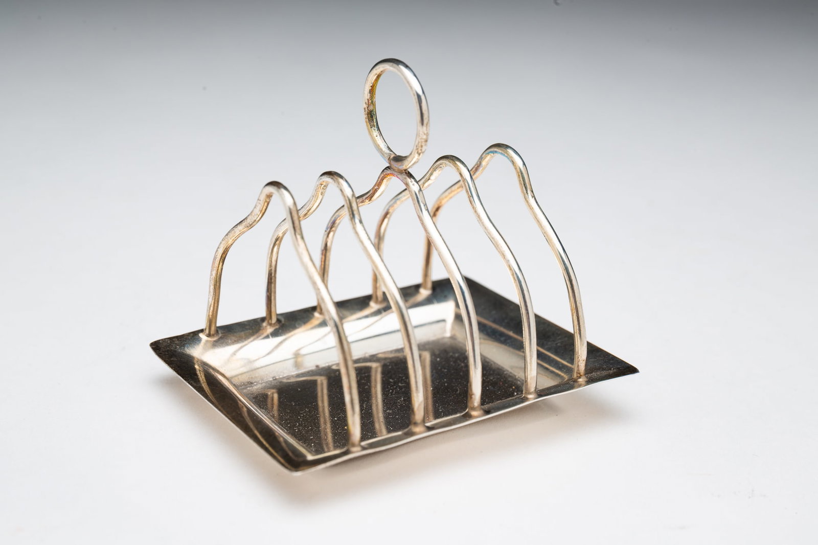 DIMINUTIVE TIFFANY & CO. STERLING SILVER TOAST TRAY.: American, 20th Century. Rectangular tray with five shaped dividers and a ring handle to top. Marked "Tiffany & Co. / Makers / Sterling / 20958 / M to bottom. 2.75"h. 2.75"w. Approximately 1.3