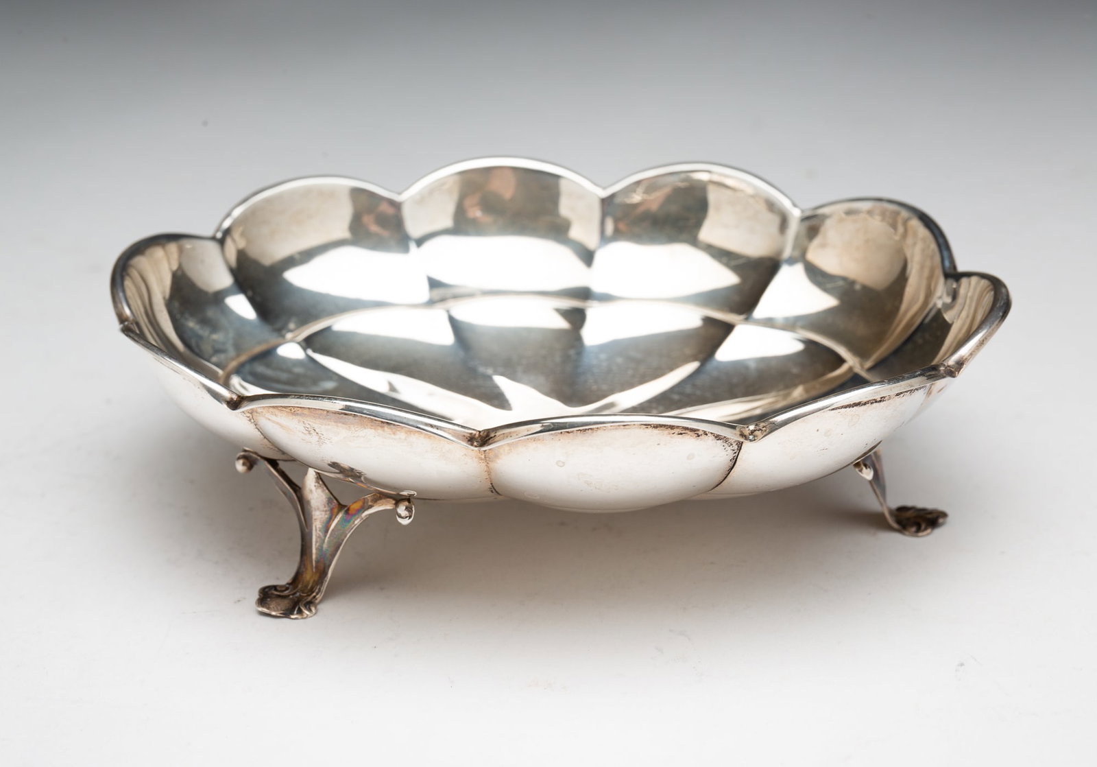 WALLACE STERLING SILVER SCALLOPED EDGE AND FOOTED DISH.: American, 20th Century. Oval dish with a shaped body, scalloped rim, and resting on three feet. 1.75"h. 5.9"w. Approximately 4.0 ozt.**Note: Bidders who are not yet established with our firm will be