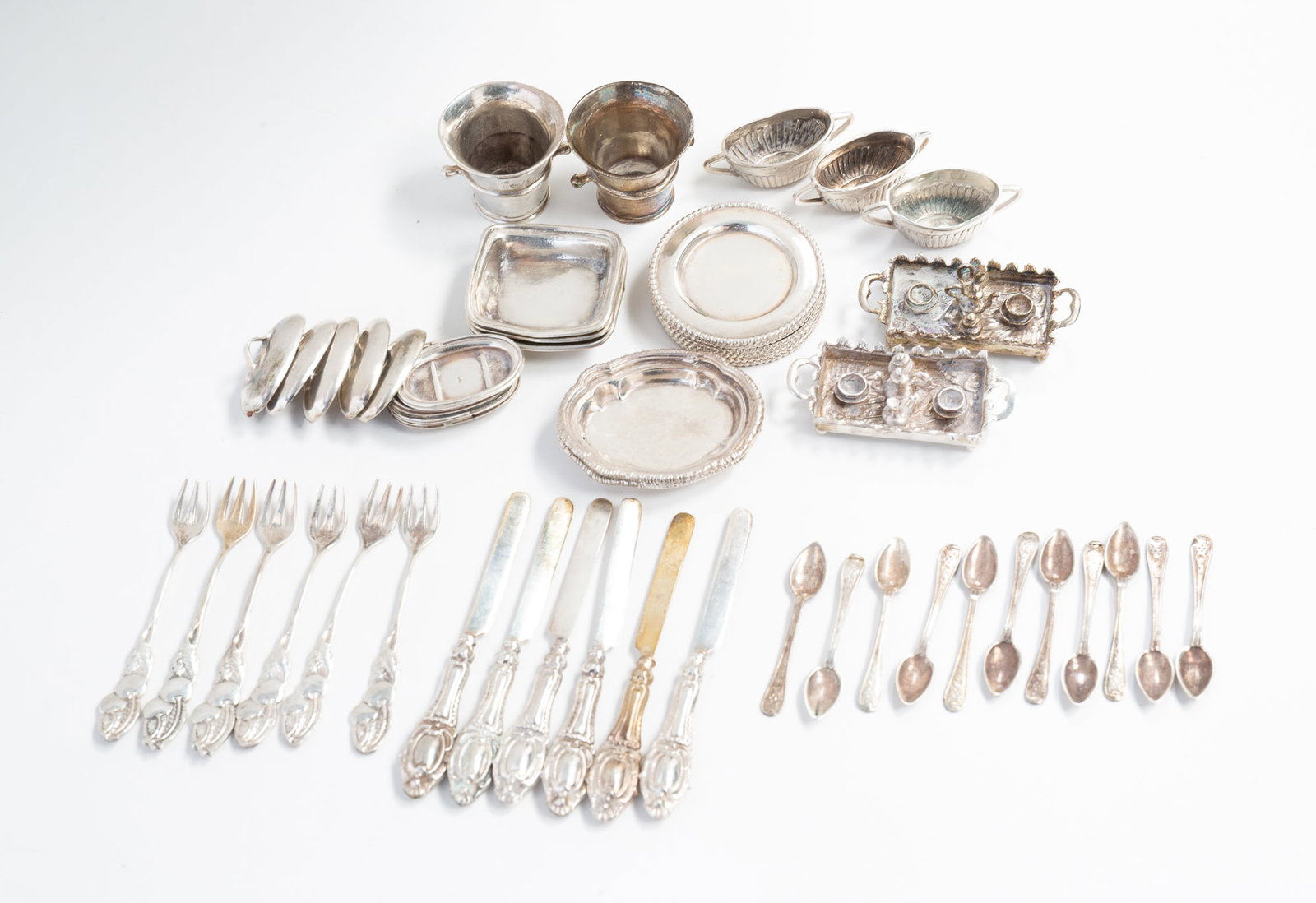 GROUP OF MINIATURE STERLING SILVER DOLLHOUSE TABLE ACCESSORIES.: English, ca. 1900. Group of miniature table accessories in sterling silver. Includes plates, platters, two tea service trays, two ice buckets, knives and forks, covered dishes, spoons, and serving