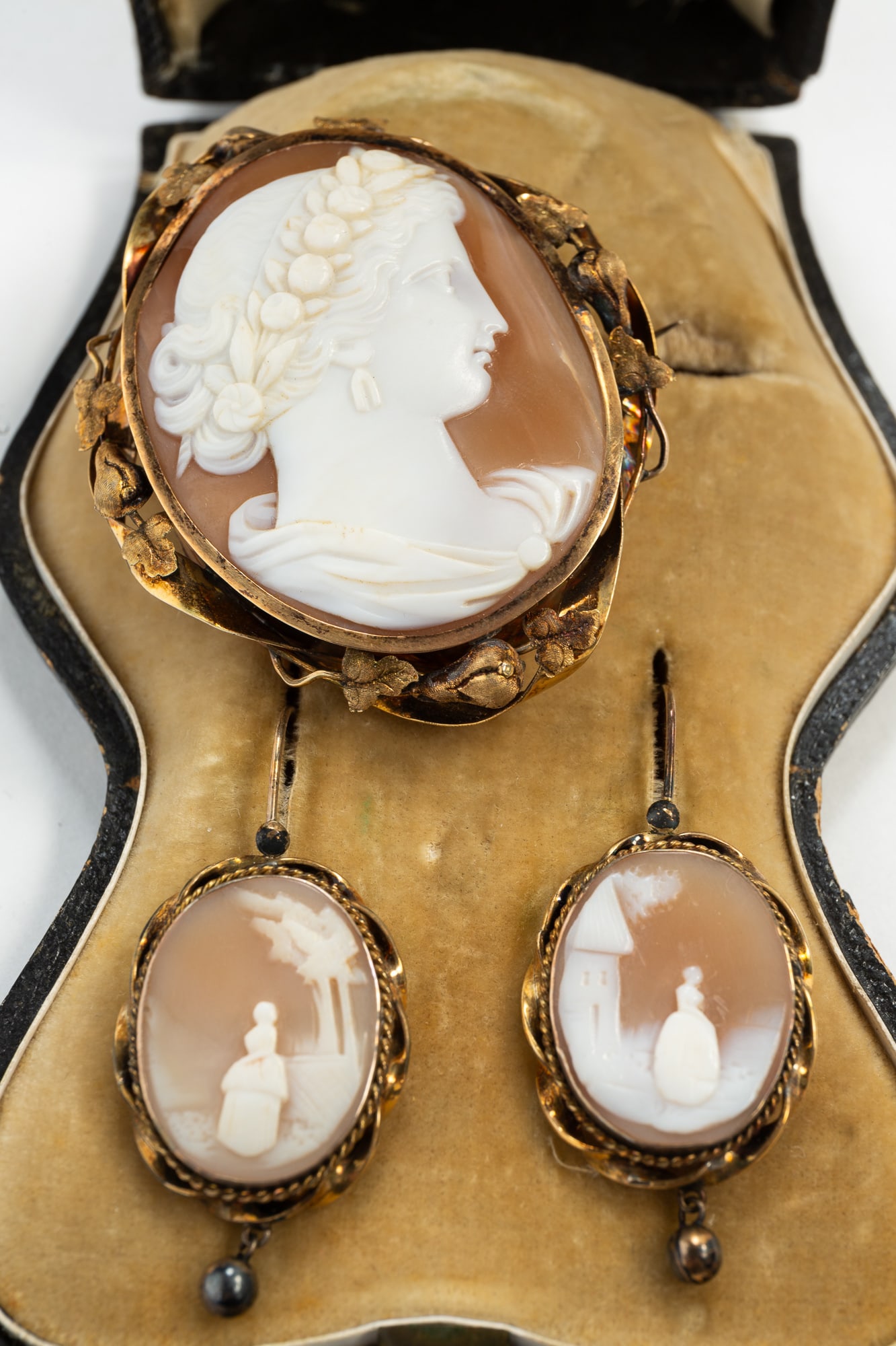 VICTORIAN CARVED SHELL CAMEO BROOCH AND EARRING SET.: Late 19th Century. A shaped box opening to reveal a large oval portrait cameo brooch with a twisted border decorated with leaves and a pair of earrings, each holding an oval carved shell cameo