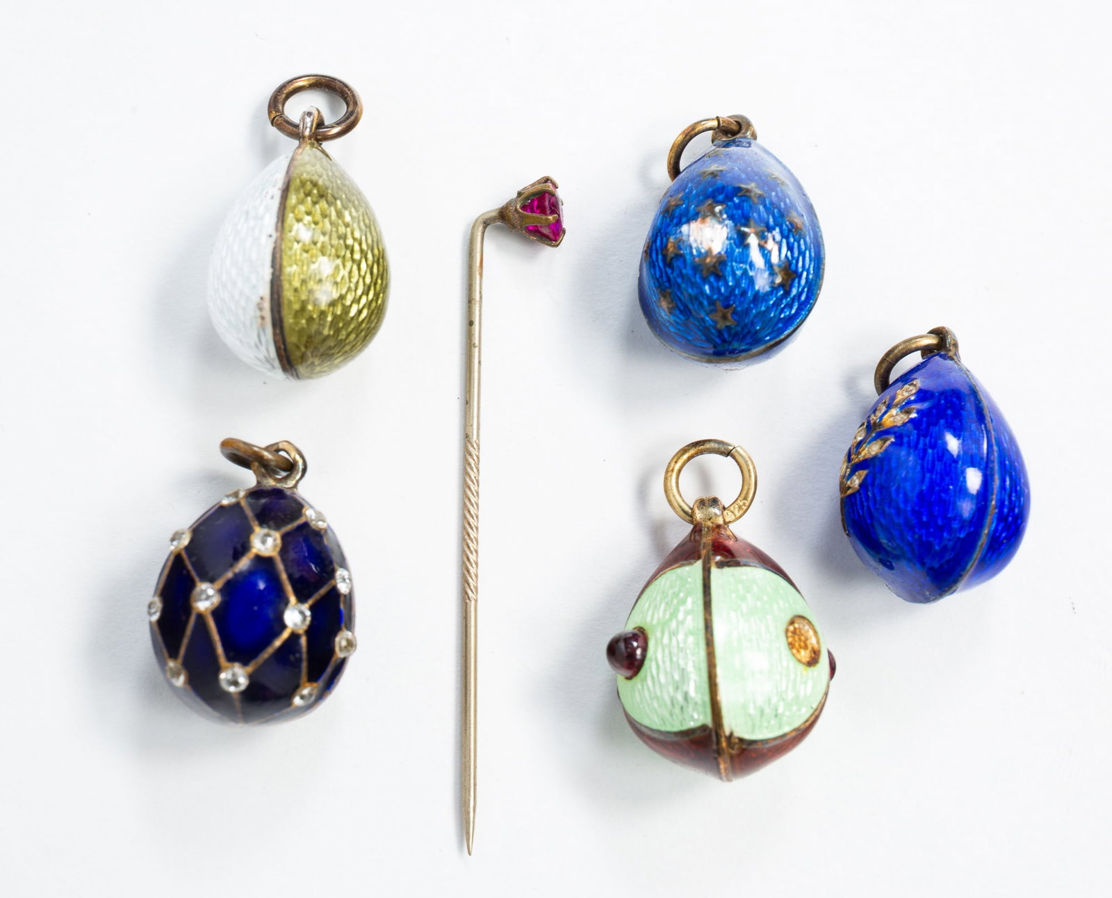 FIVE FABERGE STYLE ENAMEL EGG PENDANTS AND ONE STICK PIN.: 20th century. Each pendant featuring guilloche enamel, two with rhinestones, one with cabochon garnets, three marked '925'. Eggs measure approx. .75"l x .50"w. Enamel is in good condition. Together