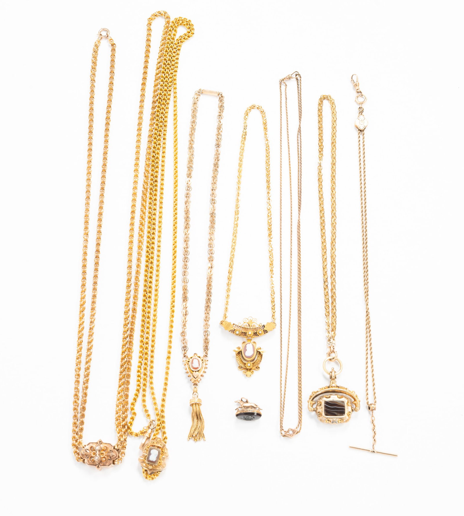GROUP OF VICTORIAN NECKLACES AND POCKETWATCH FOBS.: American, 19th Century. Gold-plated. Fobs with fancy decorated slides, featuring enamel, onyx, and opal, and two necklaces with fancy carved shell cameo pendants. Longest, 31.5"l.**Note: Bidders who