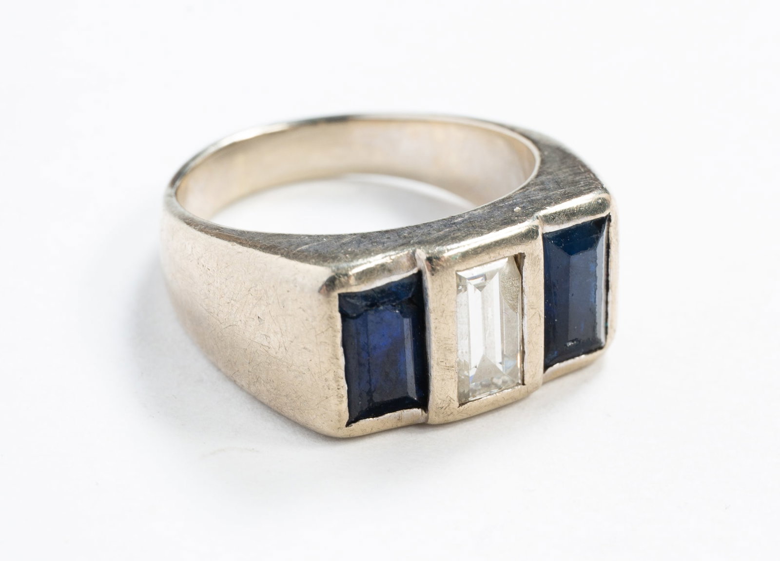 MEN'S 14K WHITE GOLD SAPPHIRE AND DIAMOND RING.: 20th Century. White gold plain band and top with two emerald-cut bezel-set sapphires around a central emerald-cut, bezel-set diamond, approx. 0.65 tcw., marked "14K", size 7. Approximately