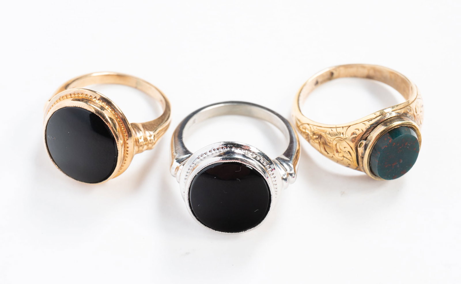 THREE 10K GOLD STONE RINGS.: 20th Century. A yellow gold ring with an oval bezel set onyx with tooled band, hallmarked, size 3.5, a yellow gold ring with brightwork at shoulders and set with an oval bloodstone, size 6.25, and a w
