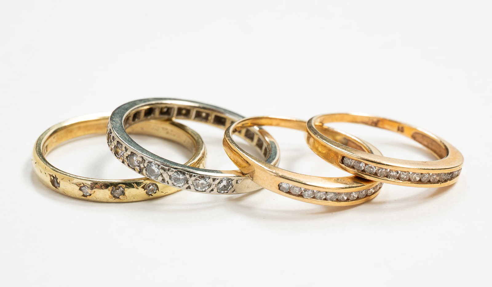 FOUR DIAMOND ETERNITY AND HALF HOOP BANDS.: American, 20th century. Four 14K gold bands to include: one 14K white gold half hoop band set with small round diamonds, Size 7; two yellow gold half hoop bands, each set with fifteen small round diam