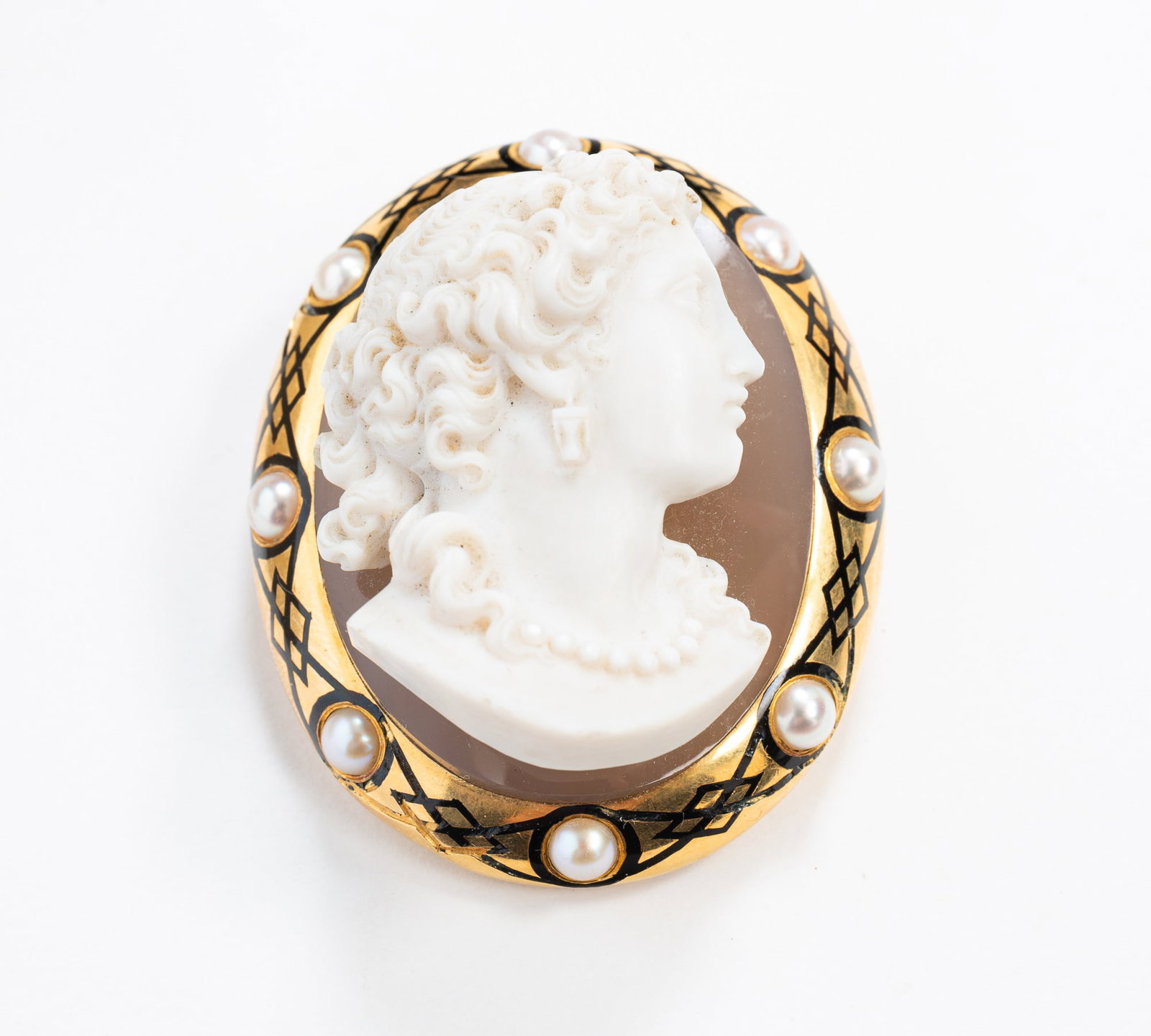 DEEPLY CARVED SHELL CAMEO SET IN 14K YELLOW GOLD BROOCH.: DEEPLY CARVED SHELL CAMEO SET IN 14K YELLOW GOLD BROOCH. 20th Century. A 14k yellow gold frame decorated with black enamel banding and eight pearls and with a deeply carved, intricate shell cameo. 2.2