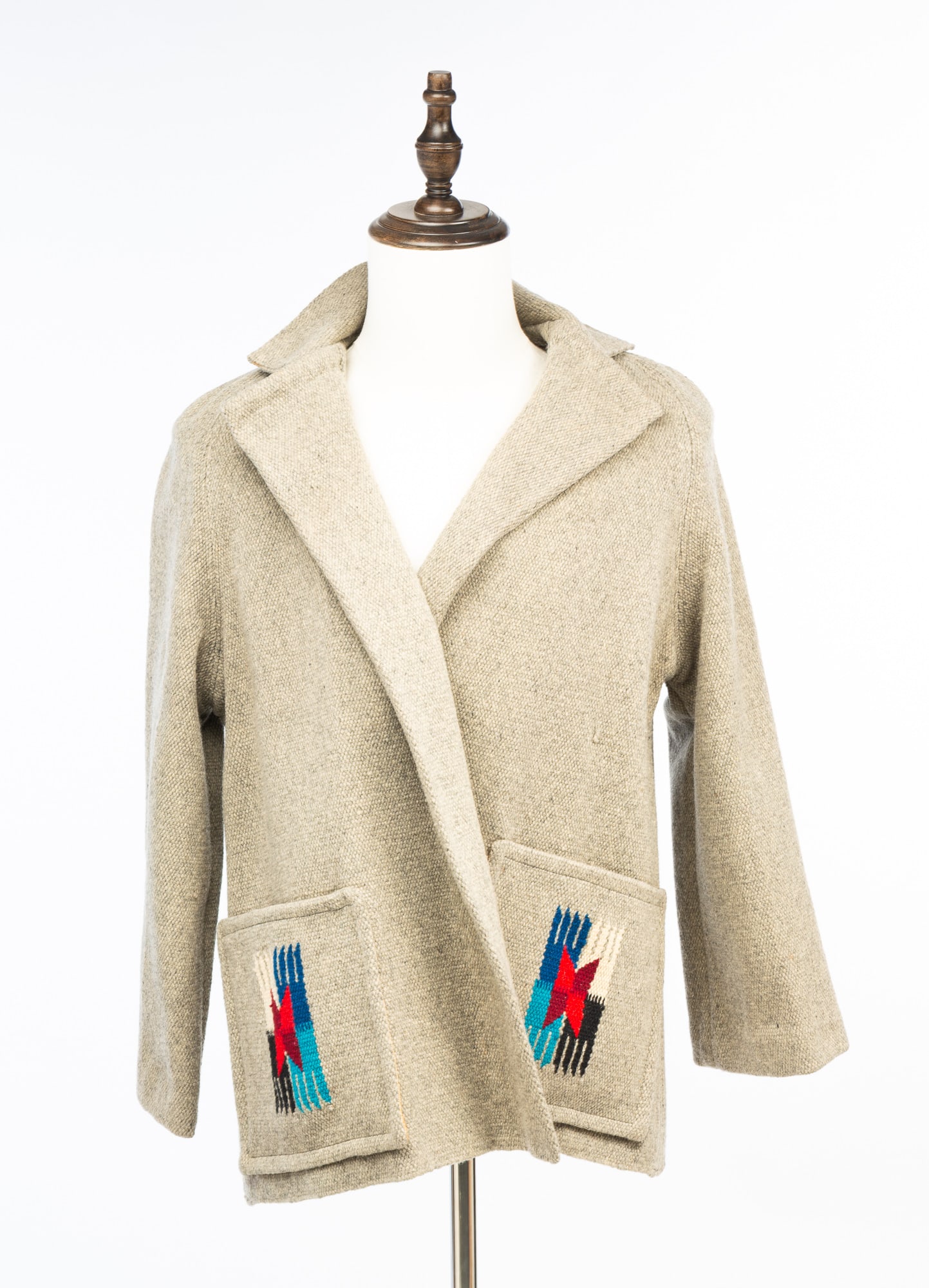 FRED HARVEY "EL GRANDEE" WOOL CHIMAYO JACKET.: Native American, Mid-20th Century. Handwoven blazer-style jacket in gray with polychrome Chimayo designs on pockets and at the center of the back. 28"l. 18" shoulder to shoulder.