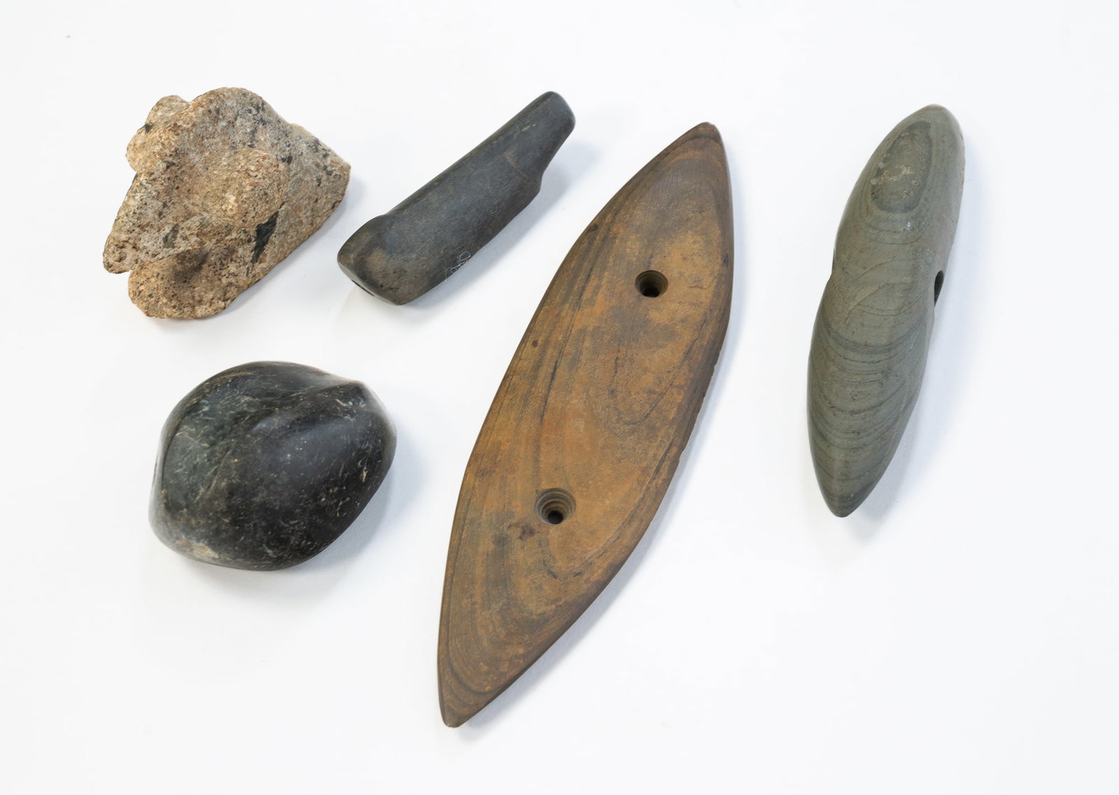 FIVE NATIVE AMERICAN STONE ITEMS FOUND IN RICHLAND COUNTY, OHIO.: FIVE NATIVE AMERICAN STONE ITEMS FOUND IN RICHLAND COUNTY, OHIO. Mottled grey and tan bird stone, 2"h. Black slate bird stone, 3"l. Elliptical gorget with two holes, 7"l. A pink banner stone in