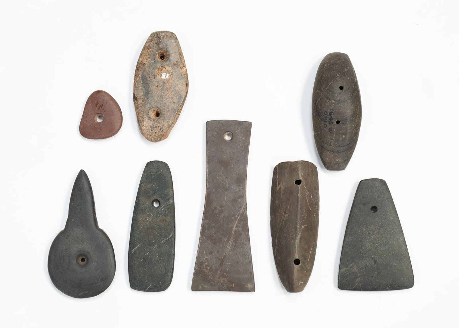 EIGHT NATIVE AMERICAN STONE GORGETS.: EIGHT NATIVE AMERICAN STONE GORGETS. Six are grey stone with one and two holes, one light grey with two holes, and lastly red with a single hole. From 5"l. to 1.25"l. 5"l.