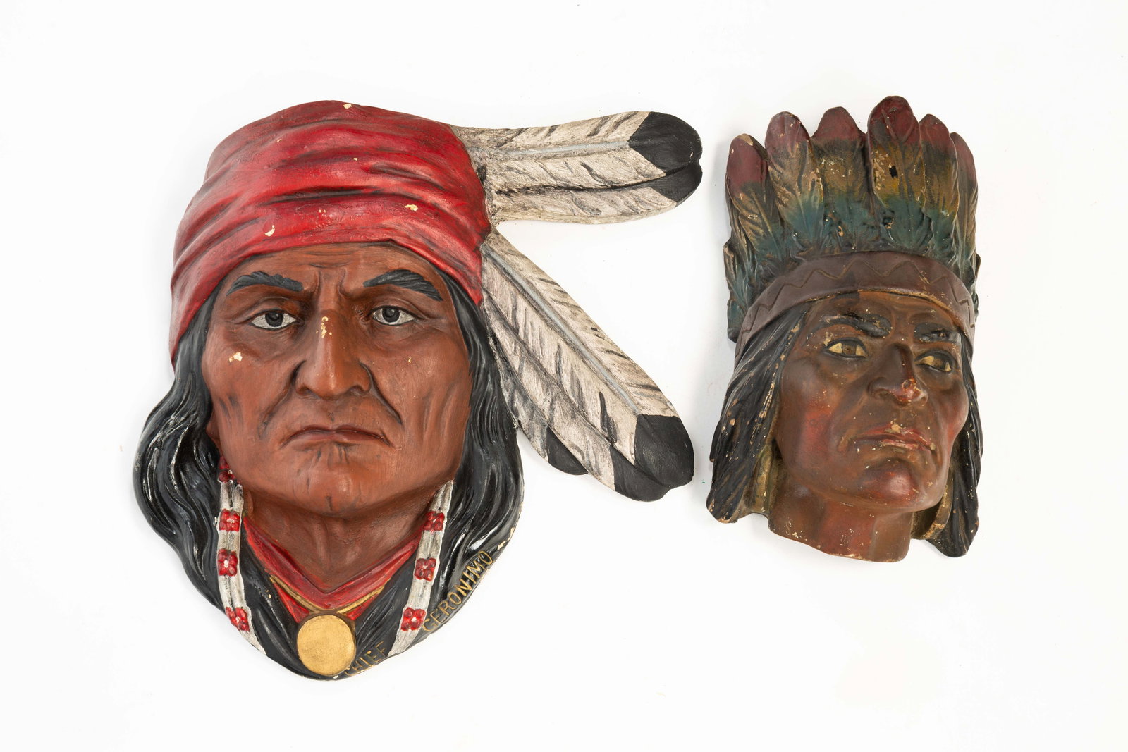 TWO PLASTER WALL PLAQUES OF NATIVE AMERICANS.: TWO PLASTER WALL PLAQUES OF NATIVE AMERICANS. American, Early 20th Century. Polychrome painted plaster of Native American faces, one depicting a man wearing a red head scarf with black and white