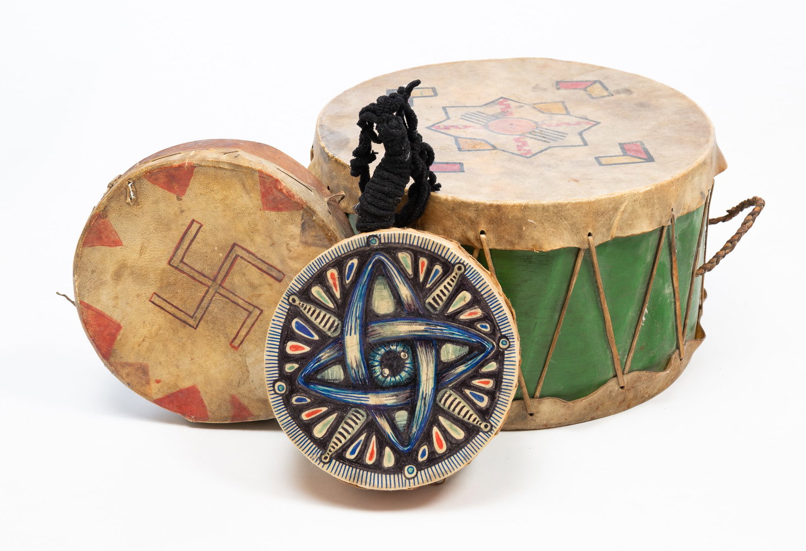 THREE NATIVE AMERICAN HIDE-COVERED DRUMS.: THREE NATIVE AMERICAN HIDE-COVERED DRUMS. 20th Century. One-sided with good luck symbol, 2.25"h. 9.25"d. Double head with black yarn handle and geometric painted head, 2.5"h. 8"d. And double-headed
