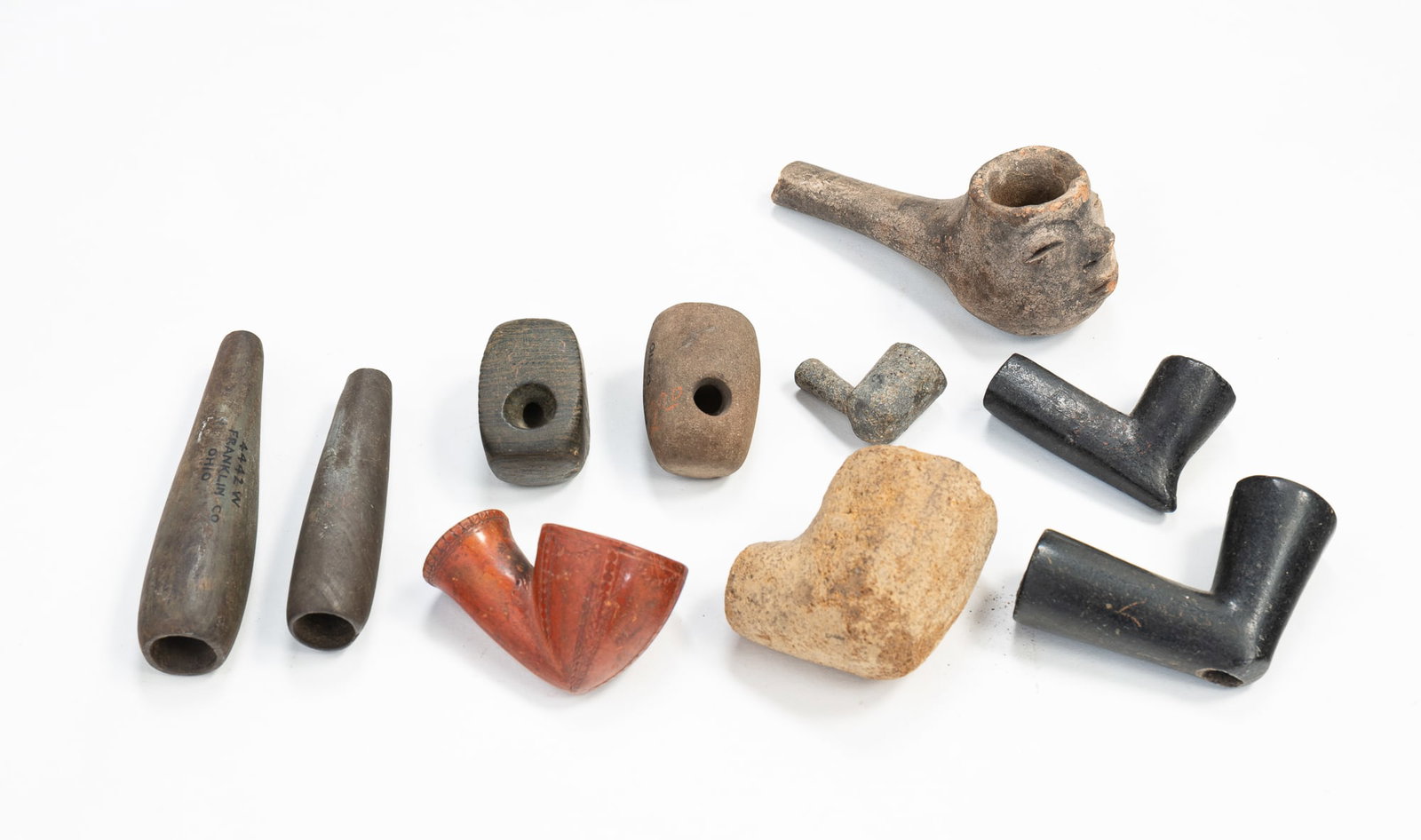 TEN NATIVE AMERICAN STONE, CLAY AND METAL PIPES.: TEN NATIVE AMERICAN STONE, CLAY AND METAL PIPES. Three are clay: red with incised decoration, 2.25", effigy face piece with broken stem, 4"w., and plain light clay, 2"w. Two are cigar-shaped: the