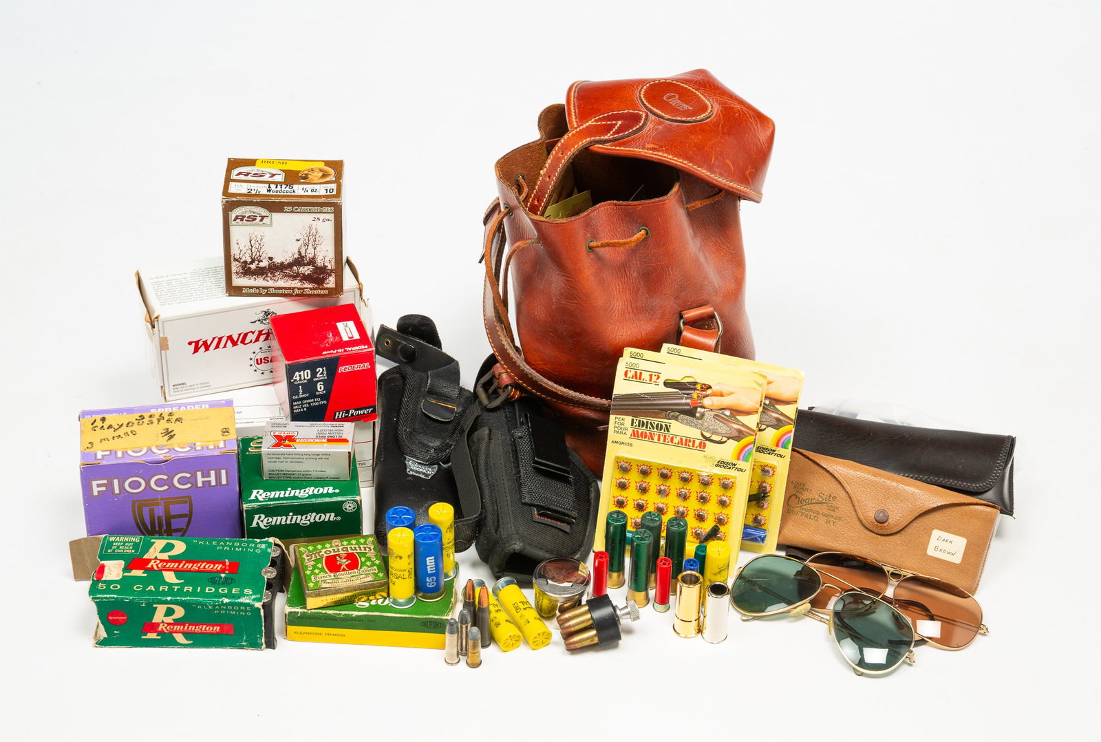 GROUP OF SHOOTING ACCESSORIES AND AMMO.: GROUP OF SHOOTING ACCESSORIES AND AMMO. American, Contemporary. Includes an Orvis leather bag, cleaning cloths, holsters, glasses, shotgun shells, .410 ammo, and various other ammo. 10"h. 12"w.